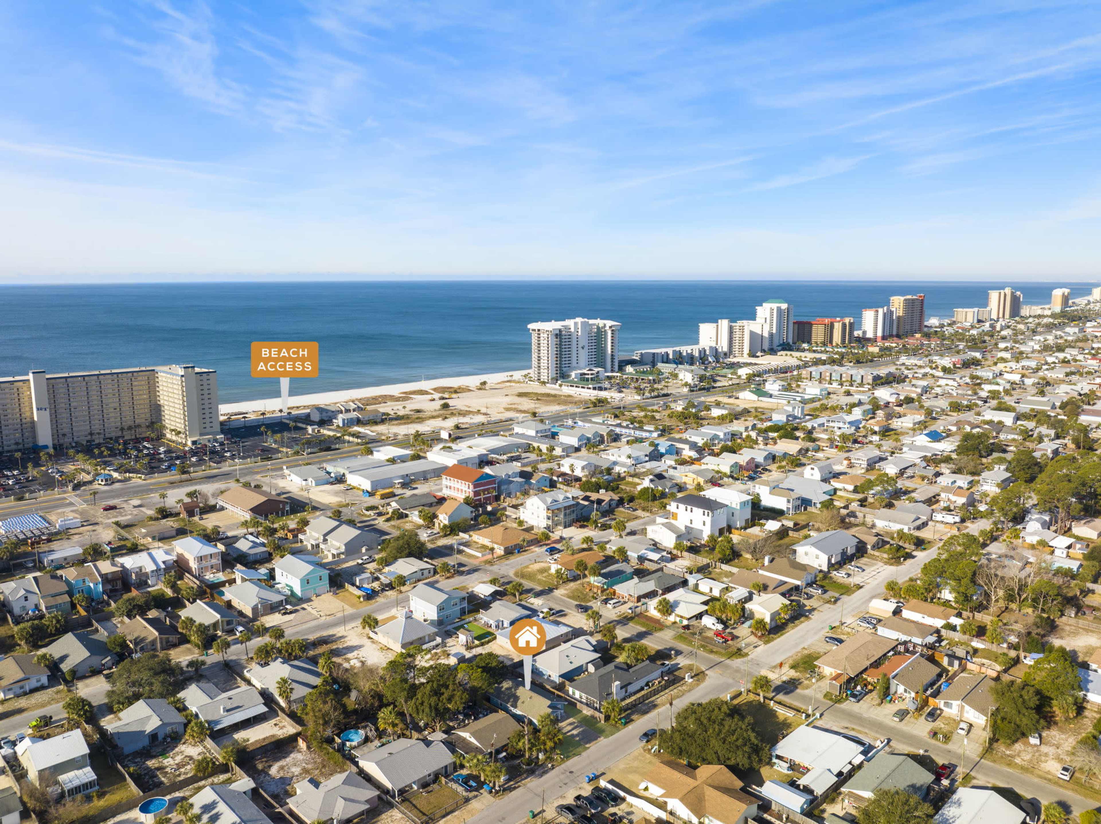 An aerial view shows a coastal area featuring a mix of residential homes and high-rise buildings, with a beach access marker visible near the shoreline.