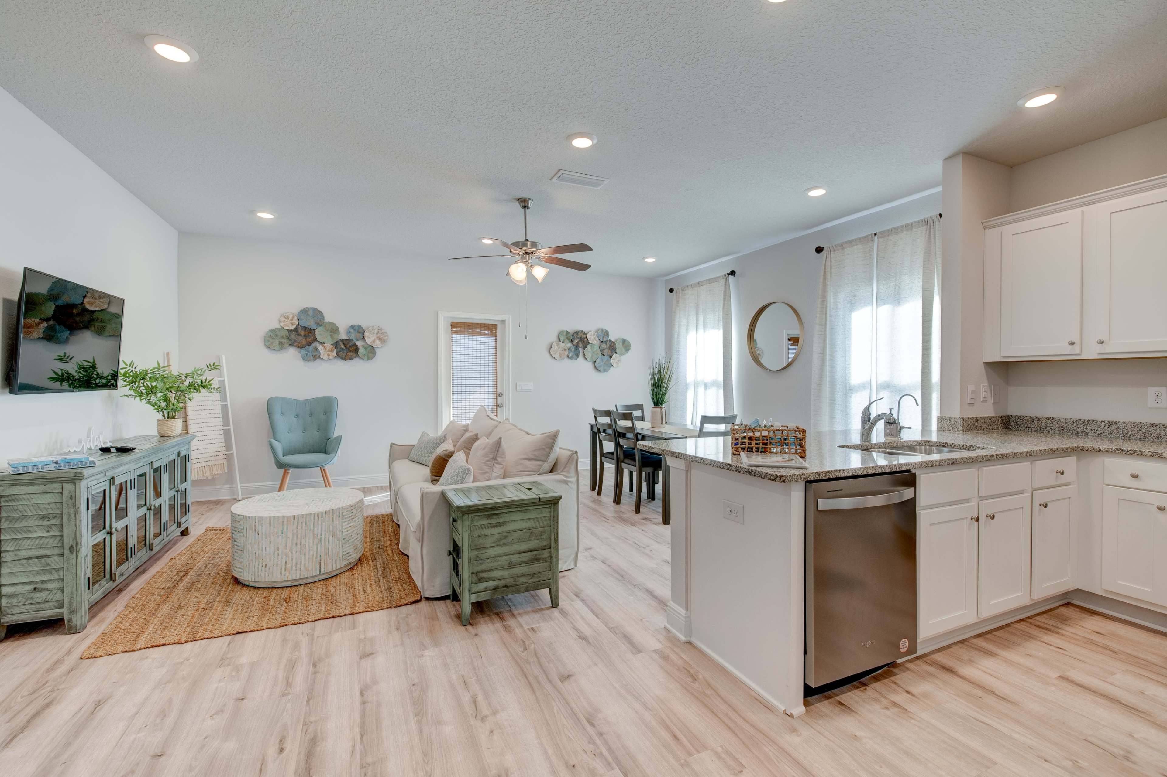 A brightly lit open-concept living area with a kitchen, dining space, and seating arrangement featuring modern furnishings and decorative elements.
