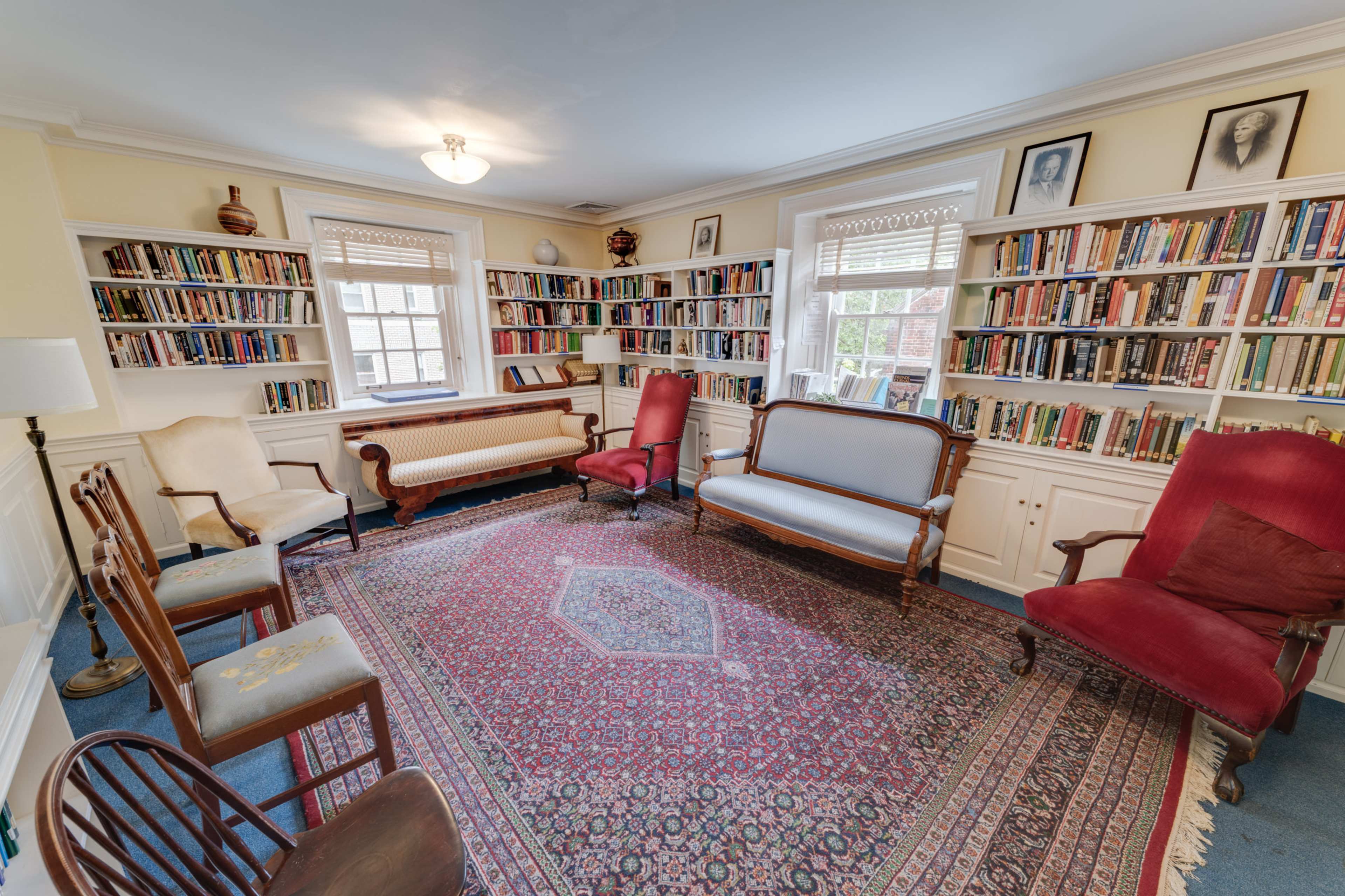A cozy library with several seating options arranged around a patterned rug and lined with bookshelves full of books.