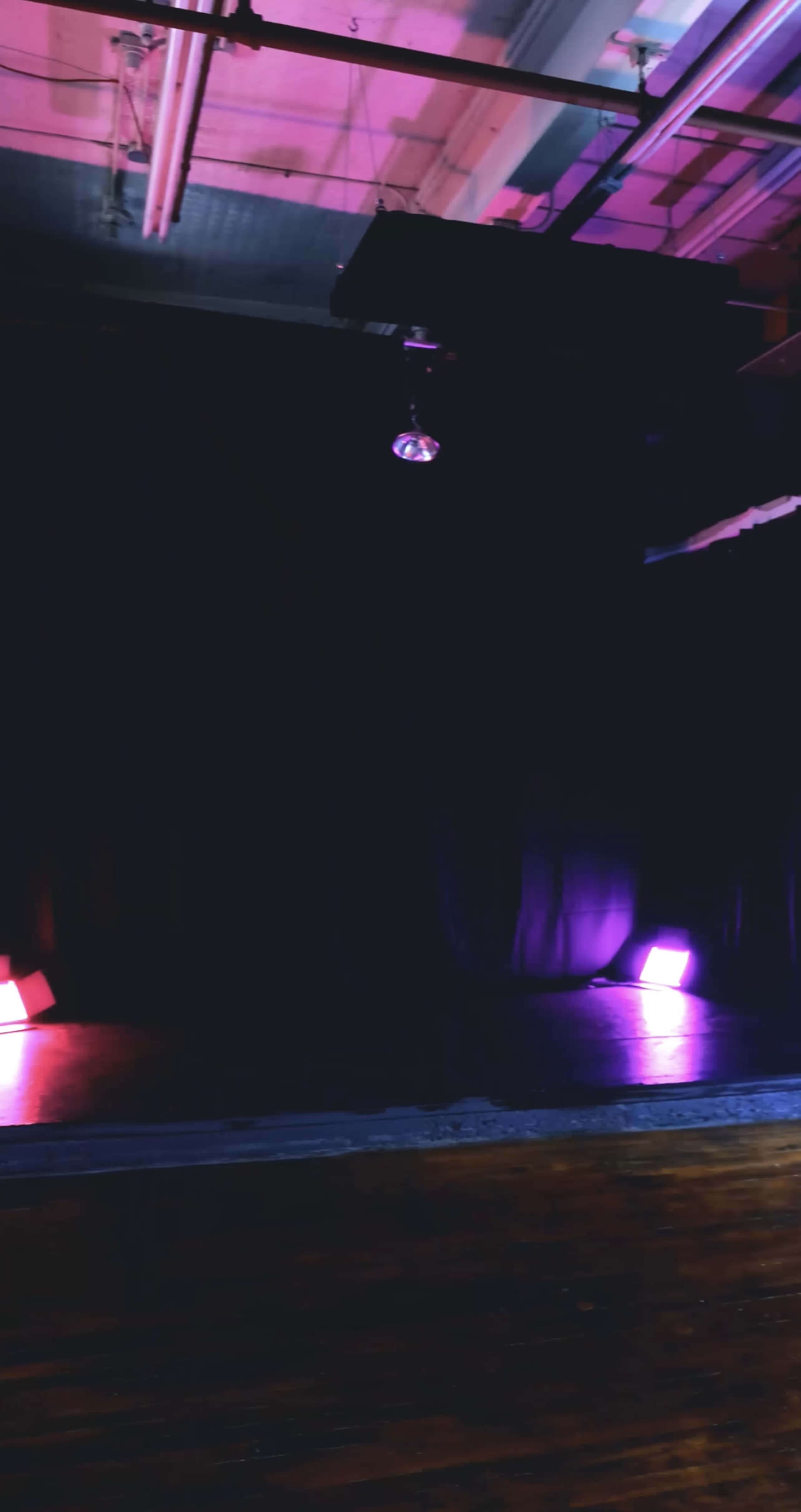 A dimly lit performance stage with purple lights on either side and a disco ball hanging from the ceiling.
