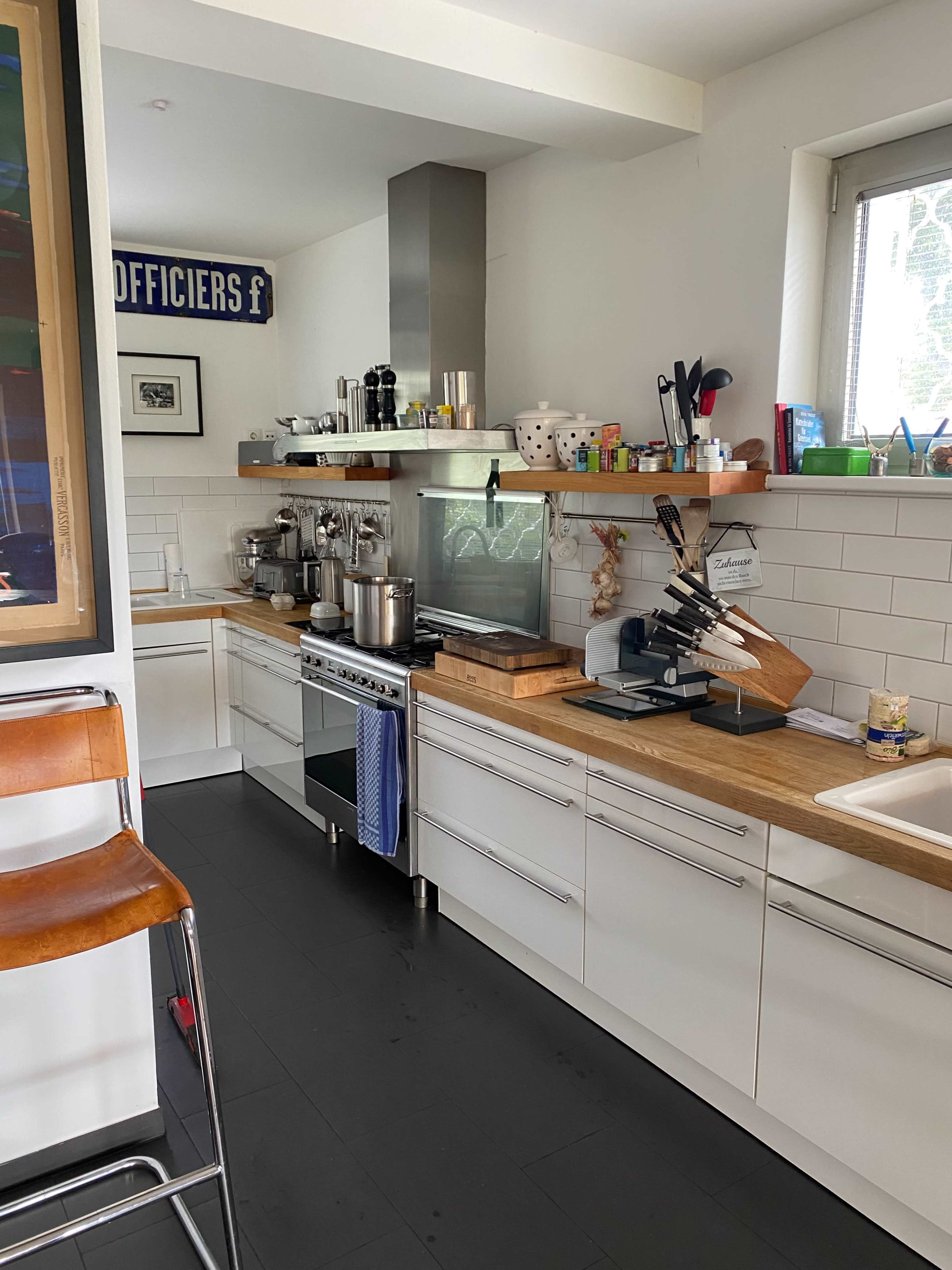 A modern kitchen with white cabinets, a stainless steel stove, and a wooden countertop, equipped with various cooking utensils and appliances.