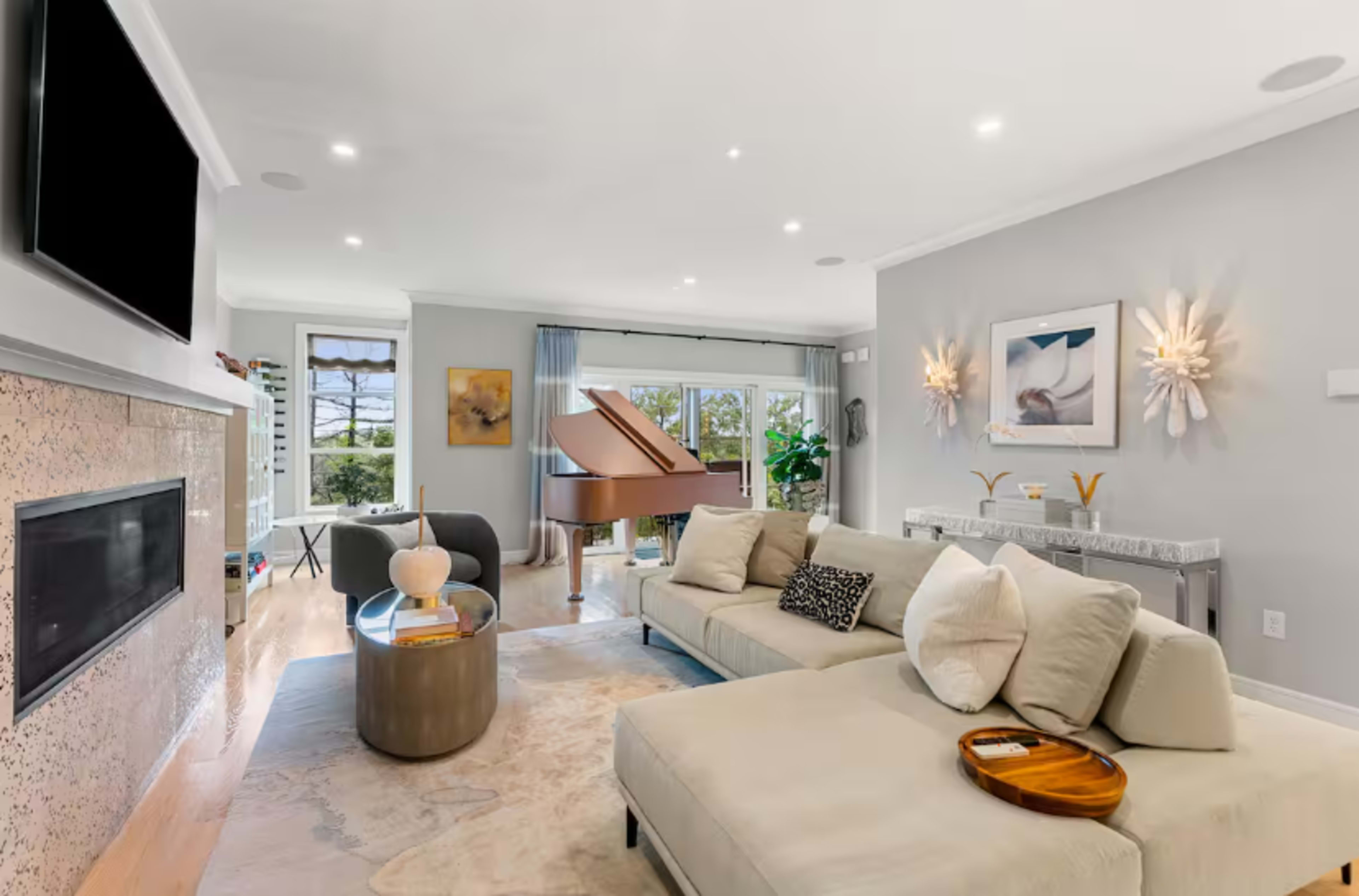 The living room features a beige sectional sofa, a round coffee table, and a grand piano near a window with light streaming in.