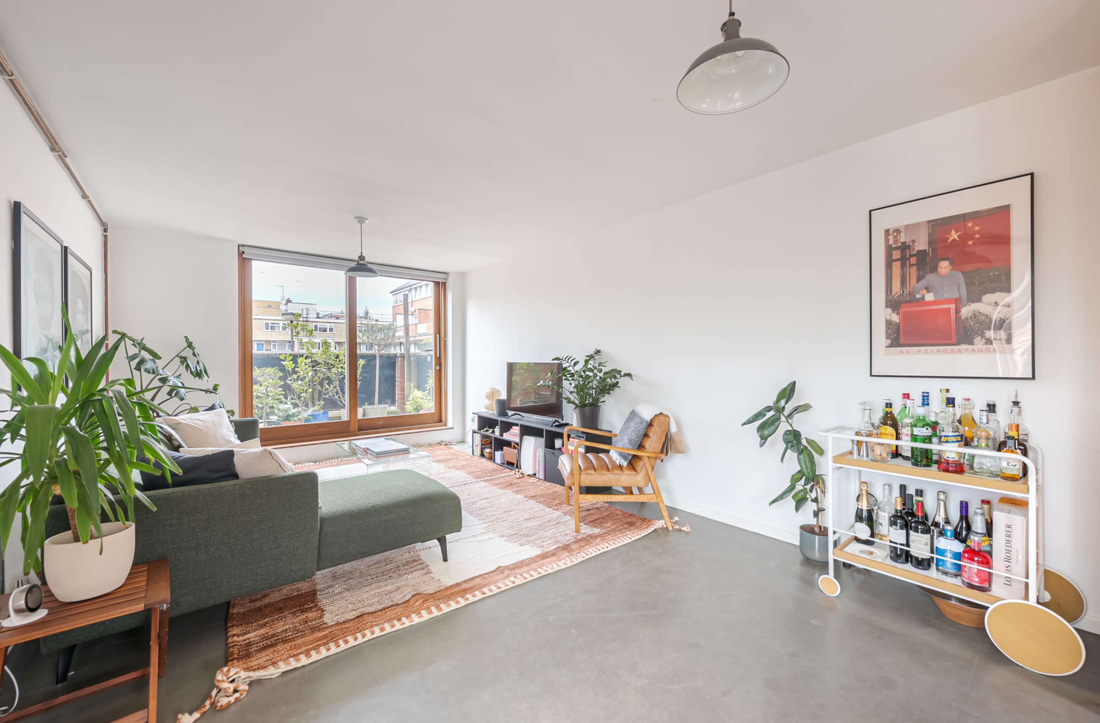 A bright living room with a green sofa, a wooden coffee table, a TV, and a beverage cart filled with various bottles.