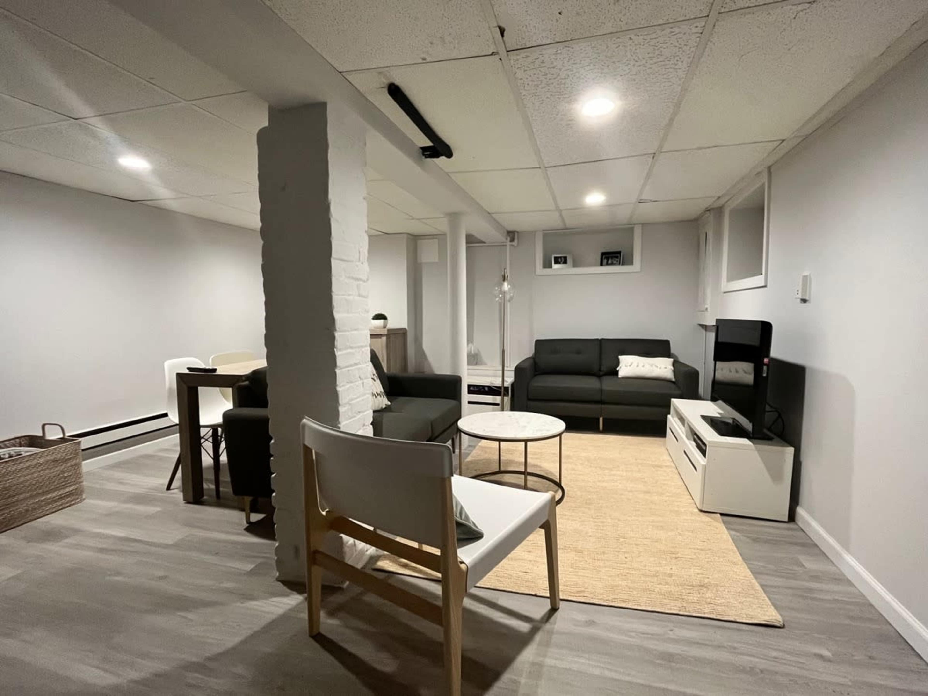 The image shows a spacious basement living area with a sectional couch, a small coffee table, a television stand, and a dining table.
