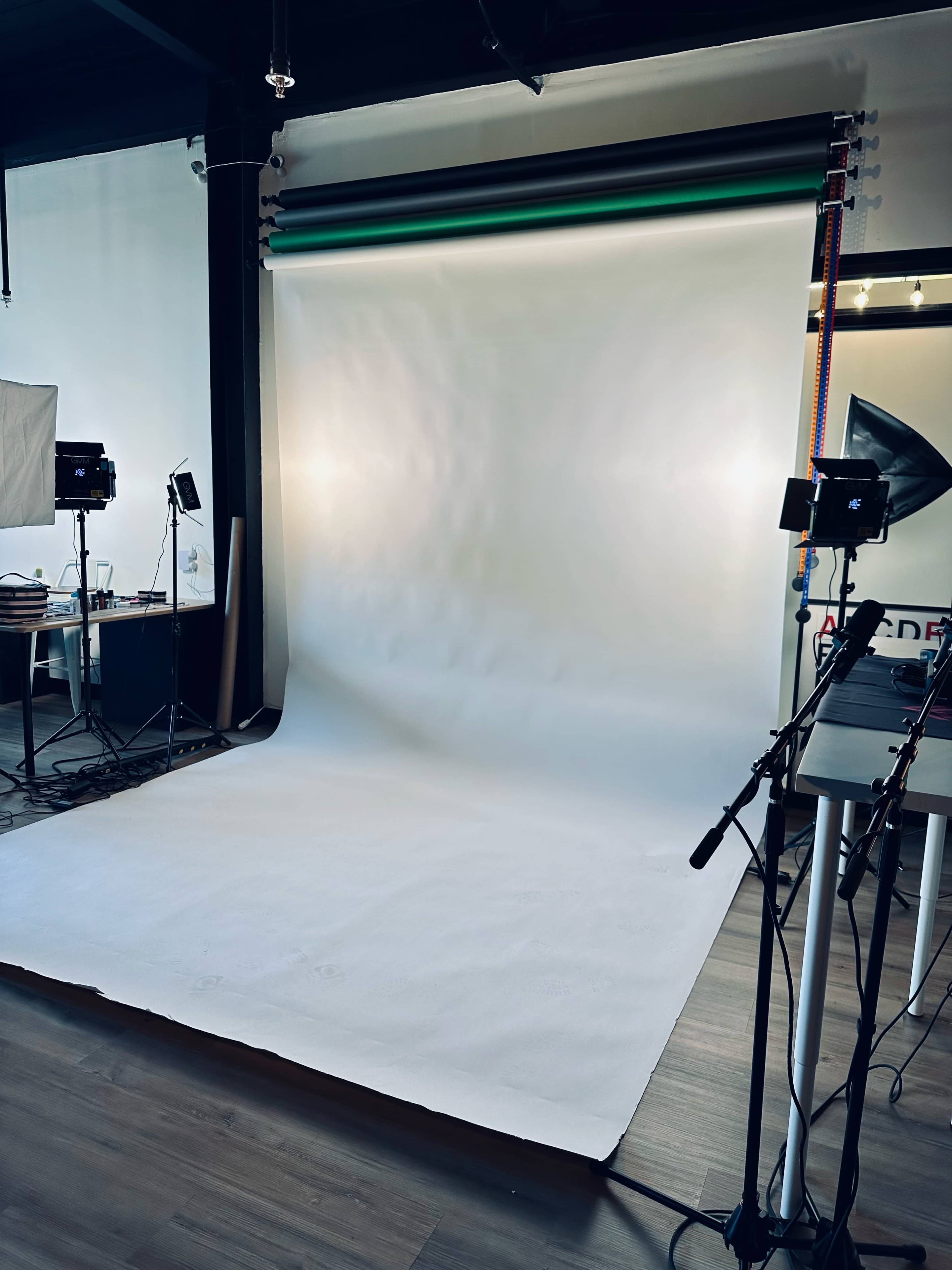 A photography studio with a white backdrop, lighting equipment, and a clean floor.
