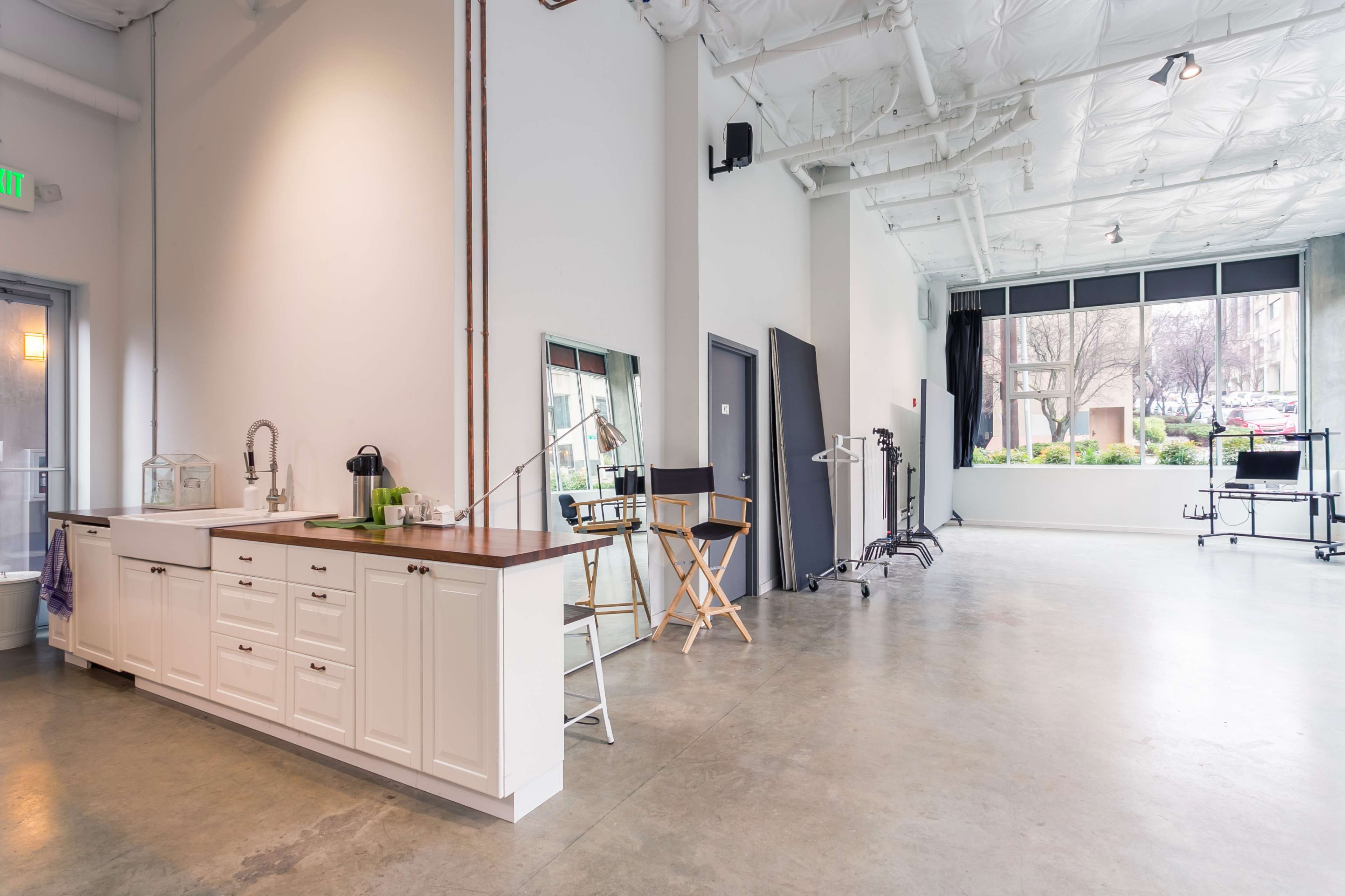 The image shows a spacious interior with a kitchen area, including a countertop and seating, alongside various work equipment in a well-lit studio space.