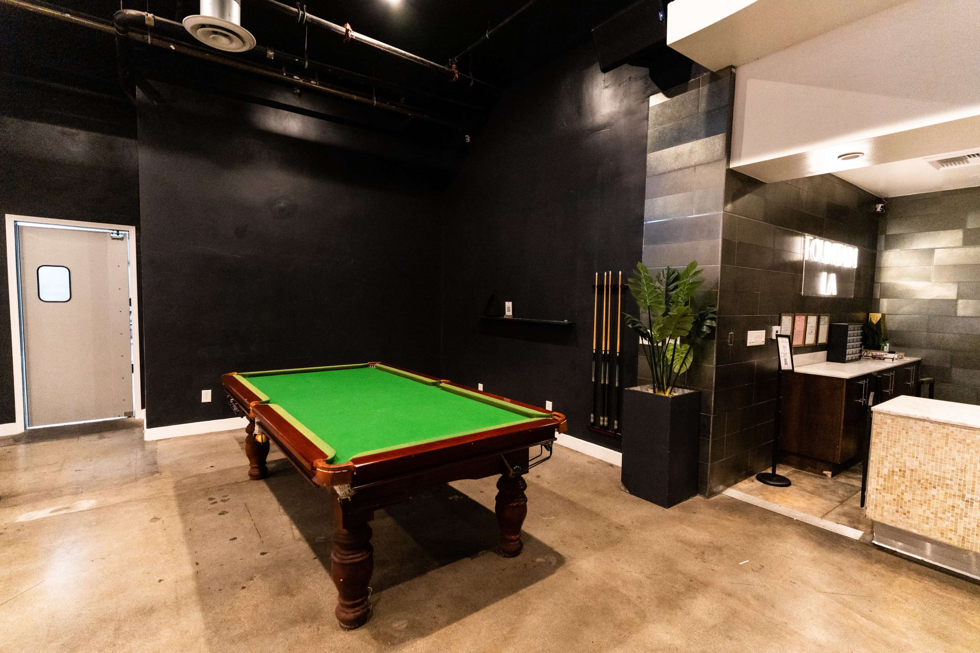 A room featuring a green billiards table, a wall with cues, and a reception area with a desk.