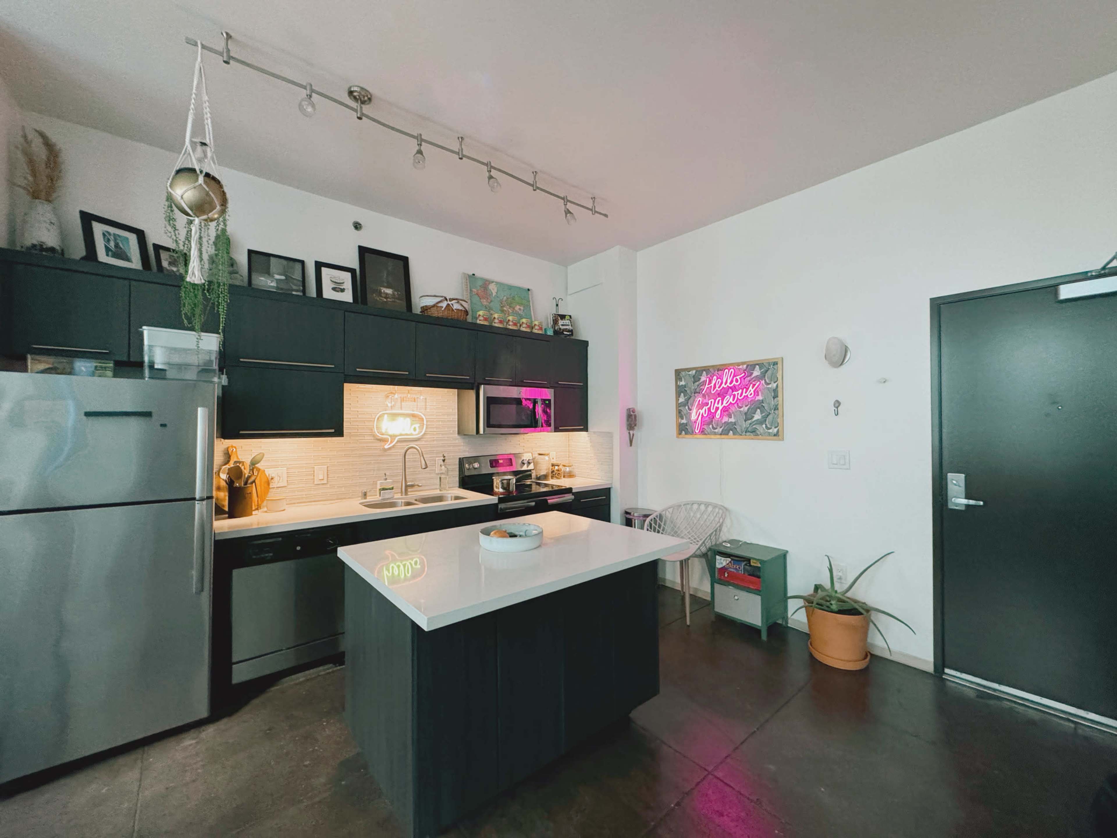 A modern kitchen features dark cabinetry, a central island with a white countertop, and decorative neon signs on the walls.