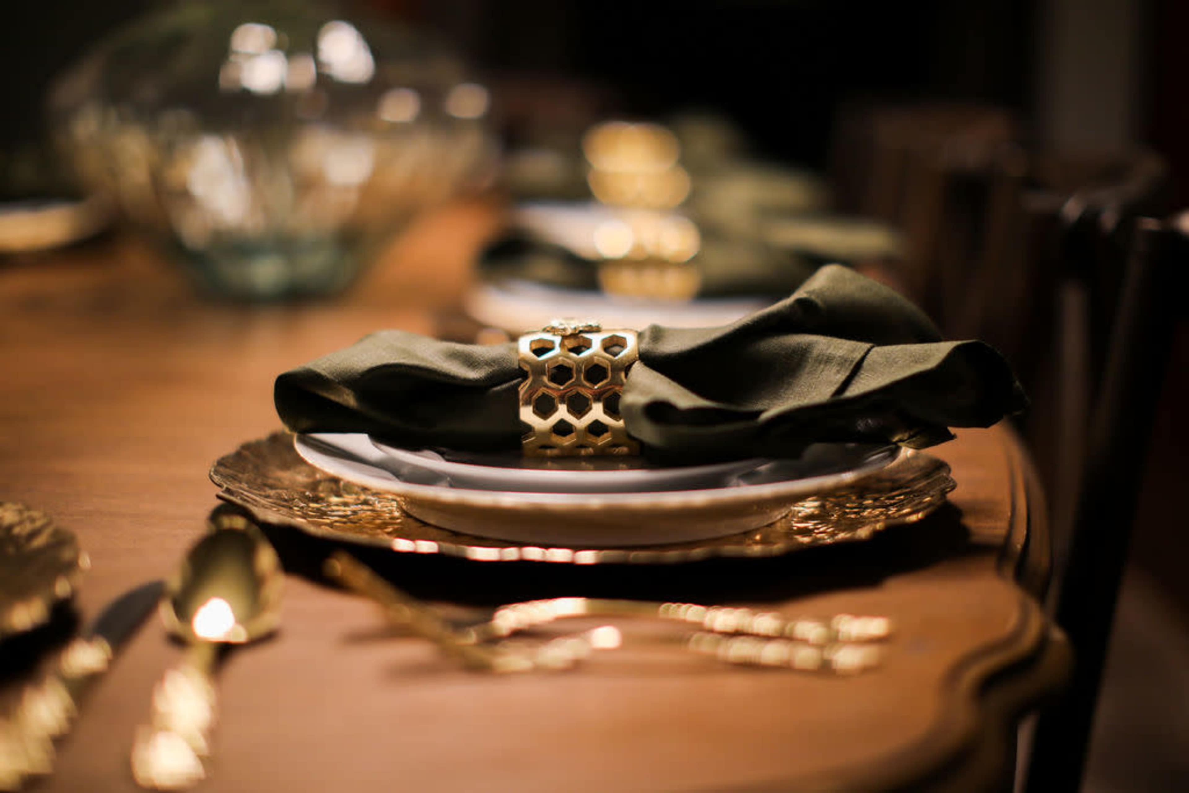 A beautifully set dining table features plates with green napkins secured by decorative gold rings, surrounded by elegant cutlery.