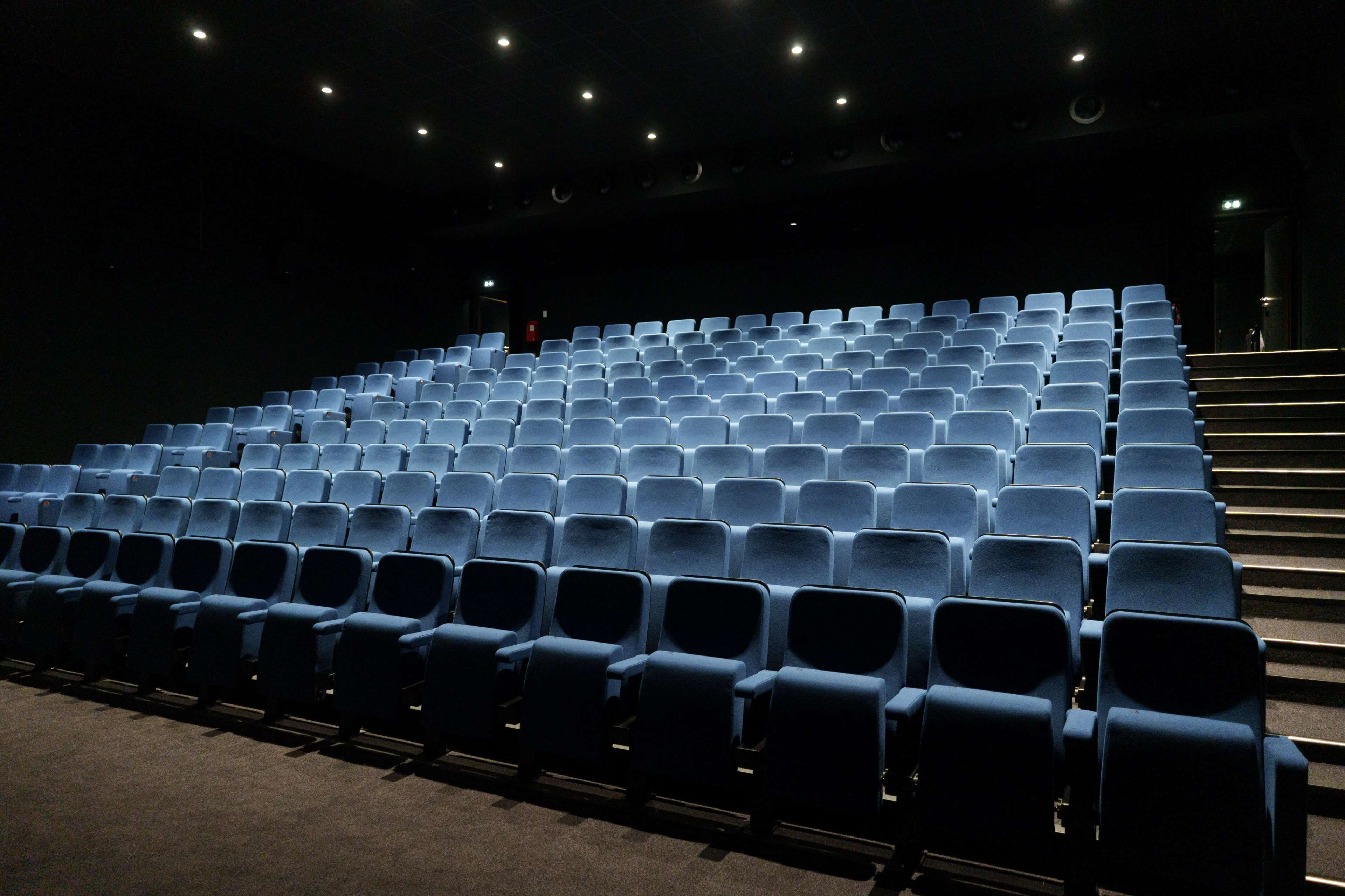 A nearly empty movie theater with rows of blue upholstered seats arranged in a sloped format.