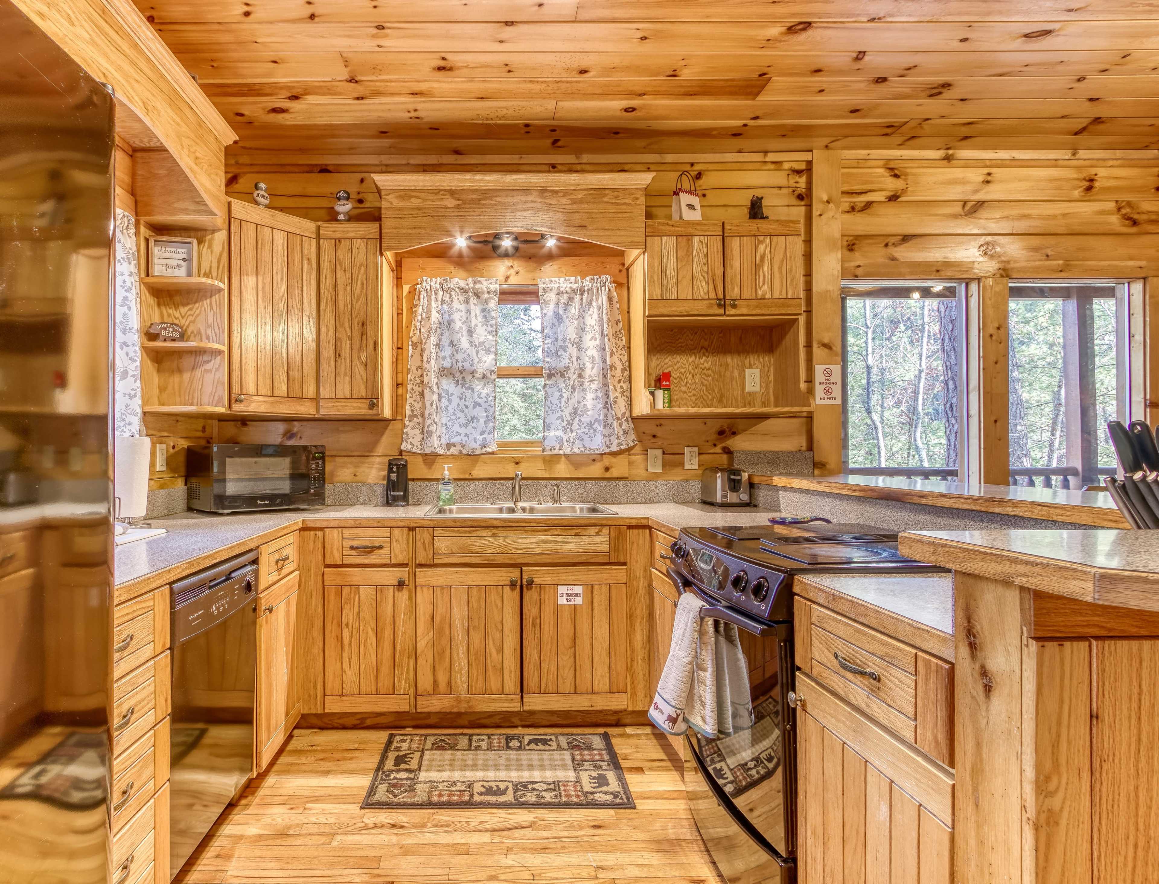 A wooden cabin kitchen with light wood cabinets, a stove, and a window offering a view of the outdoors.