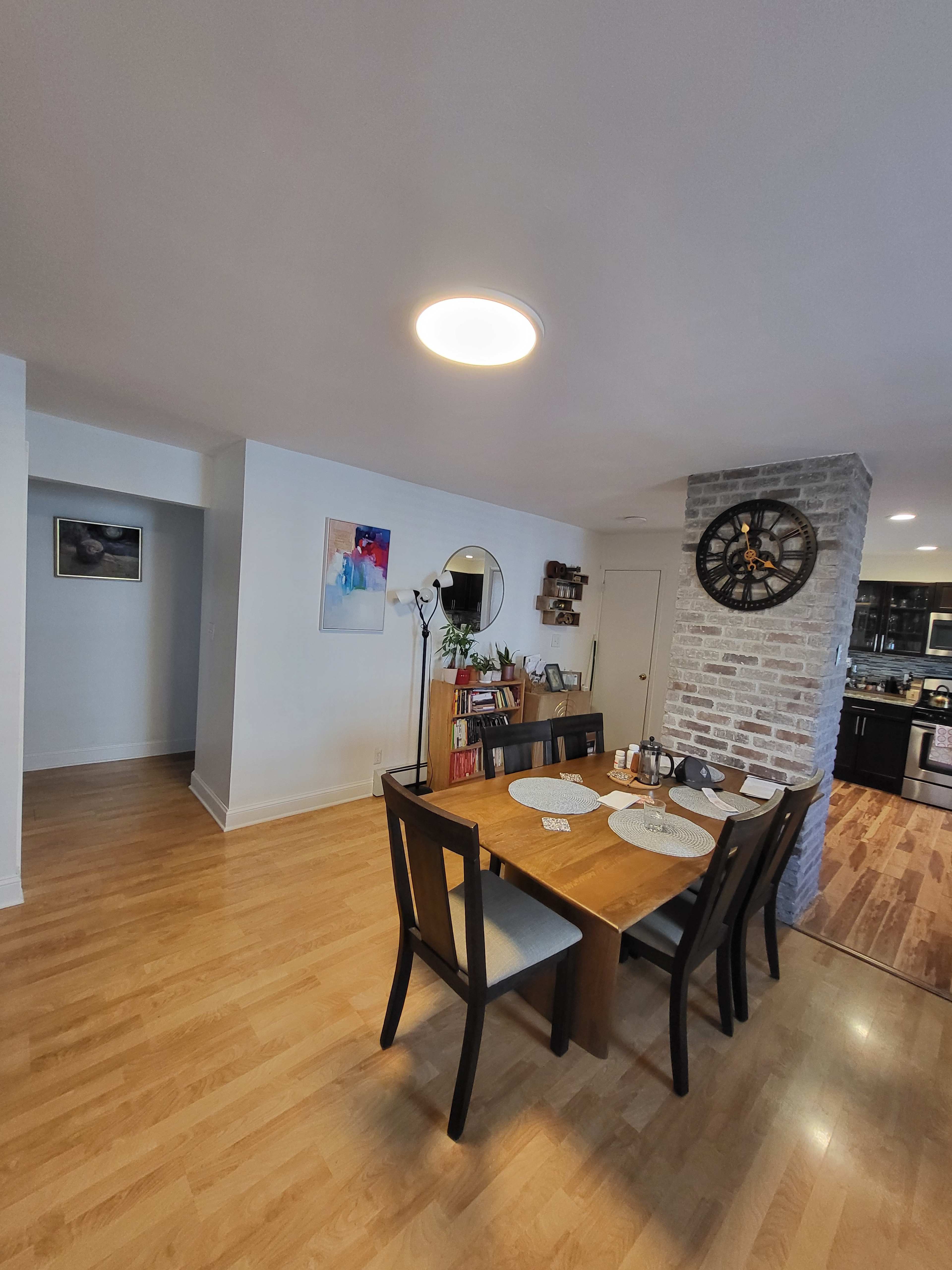 The image shows a modern dining area with a wooden table set for five, surrounded by chairs, and a wall partition featuring a stone texture.