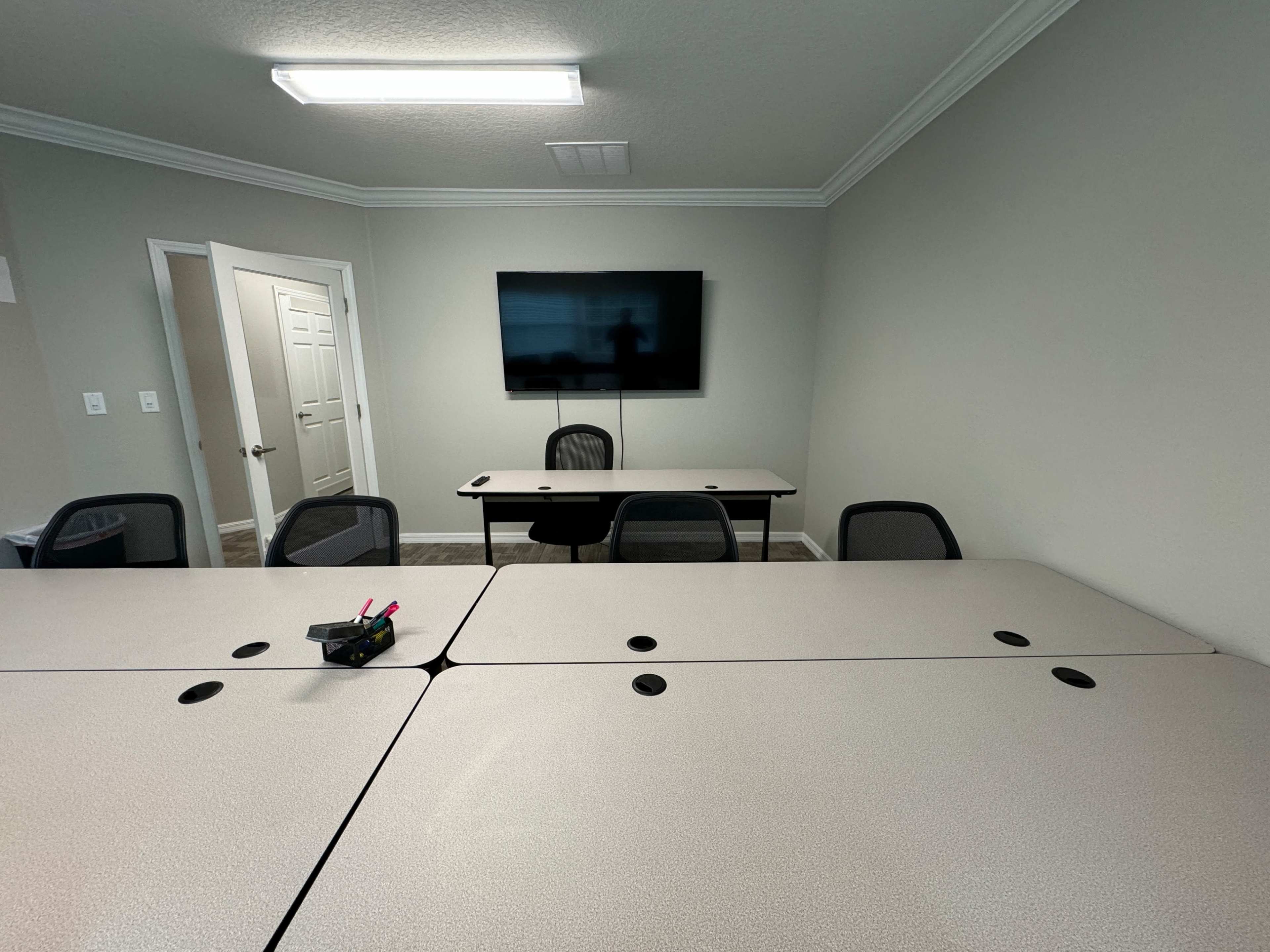 A clean conference room with a table and several chairs facing a wall-mounted television.