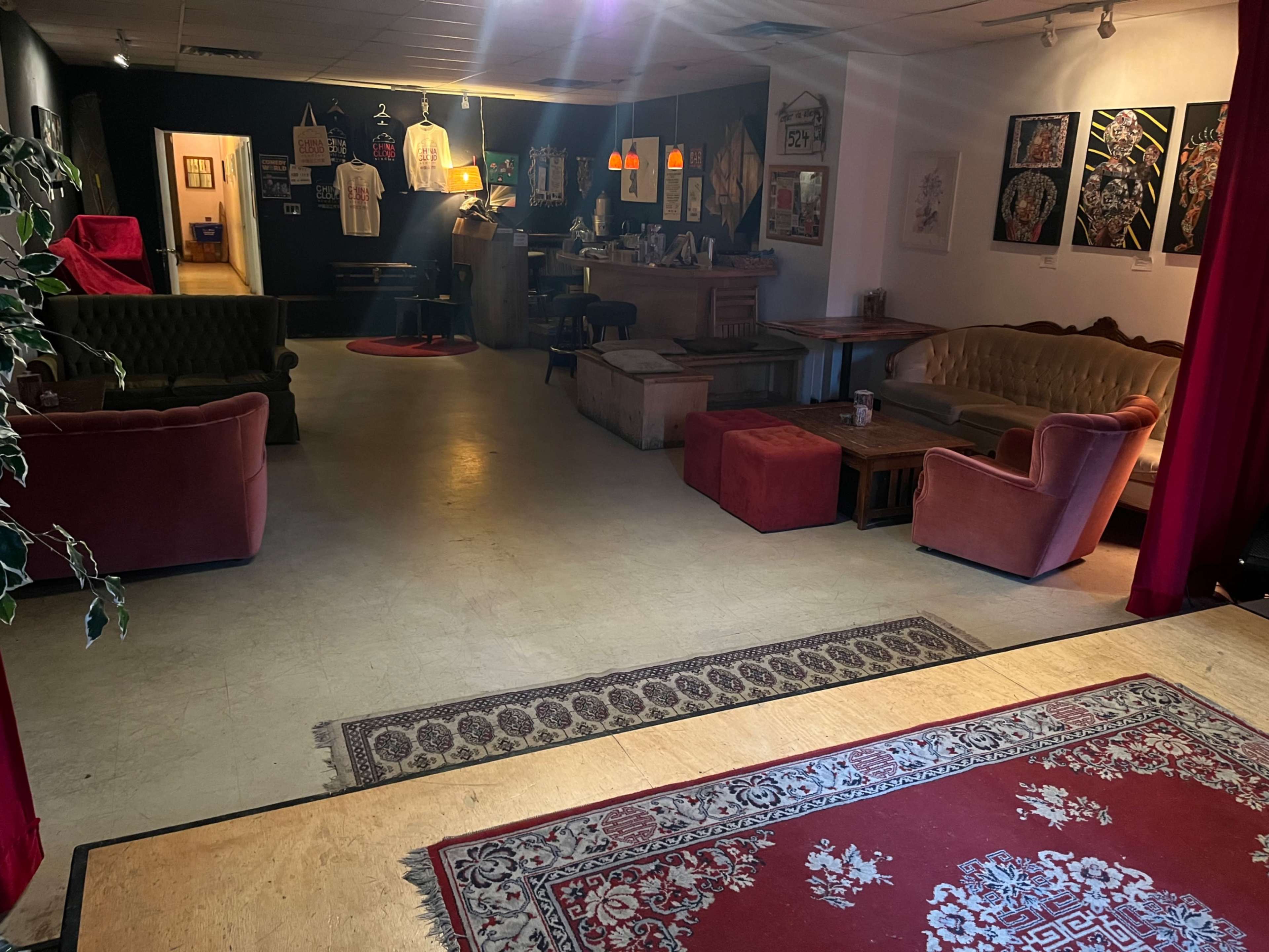 The image shows a cozy interior space featuring multiple seating areas, a small bar, and decorative art on the walls.