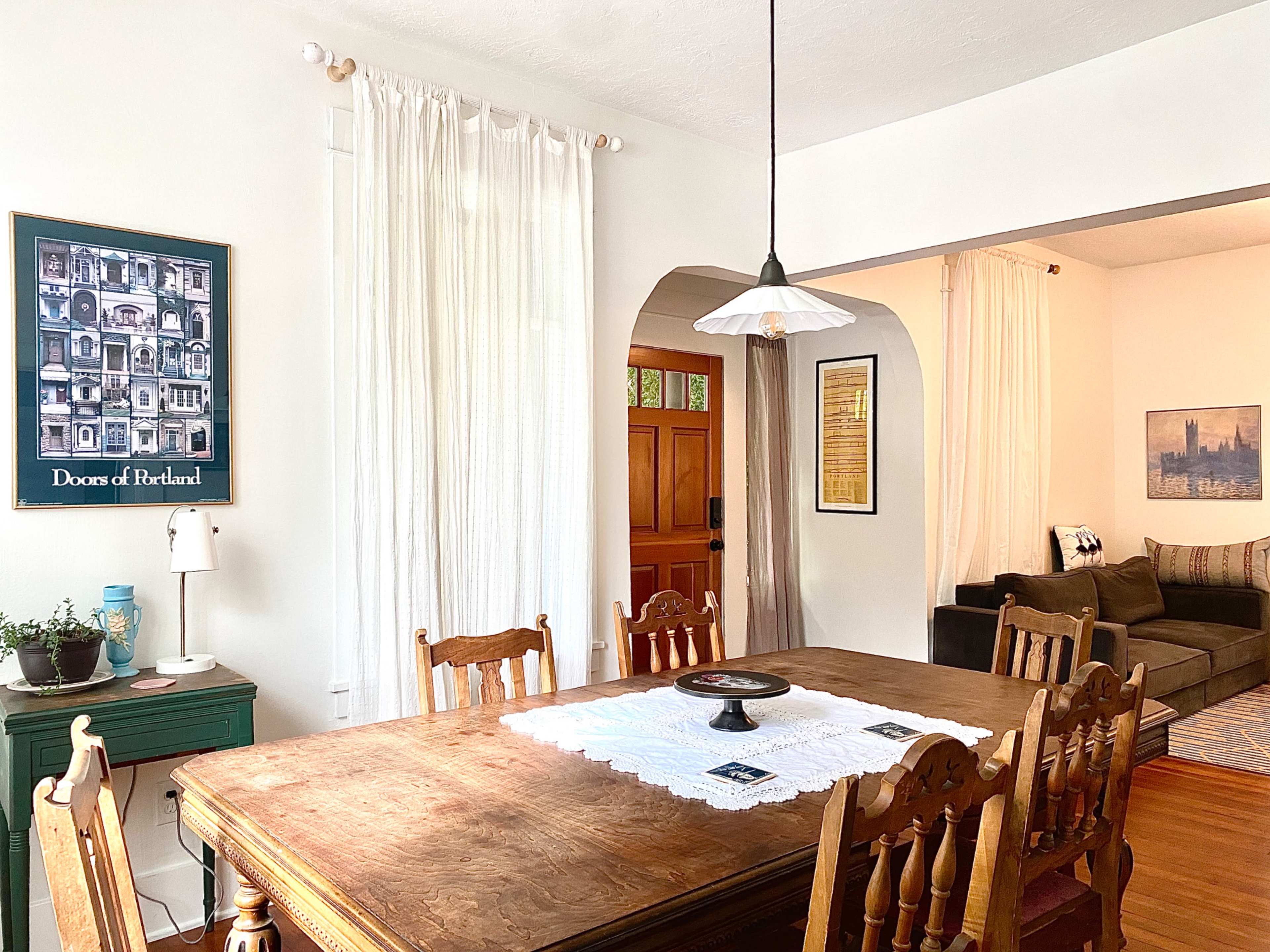 The image features a dining area with a wooden table surrounded by chairs, illuminated by a pendant light, and an adjoining room visible in the background.