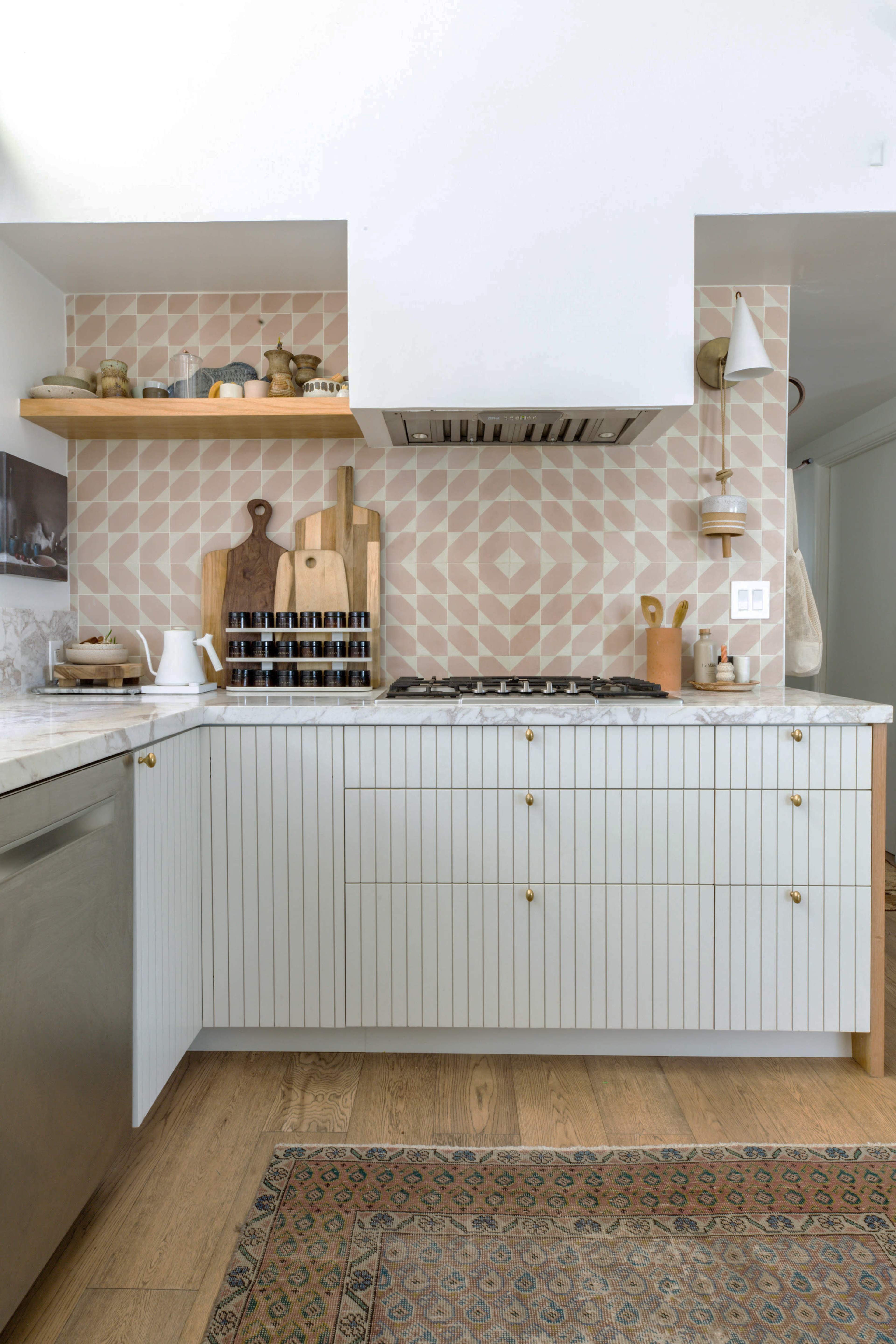 The image shows a modern kitchen with a gas stove, white cabinetry featuring vertical lines, and a pink patterned backsplash.