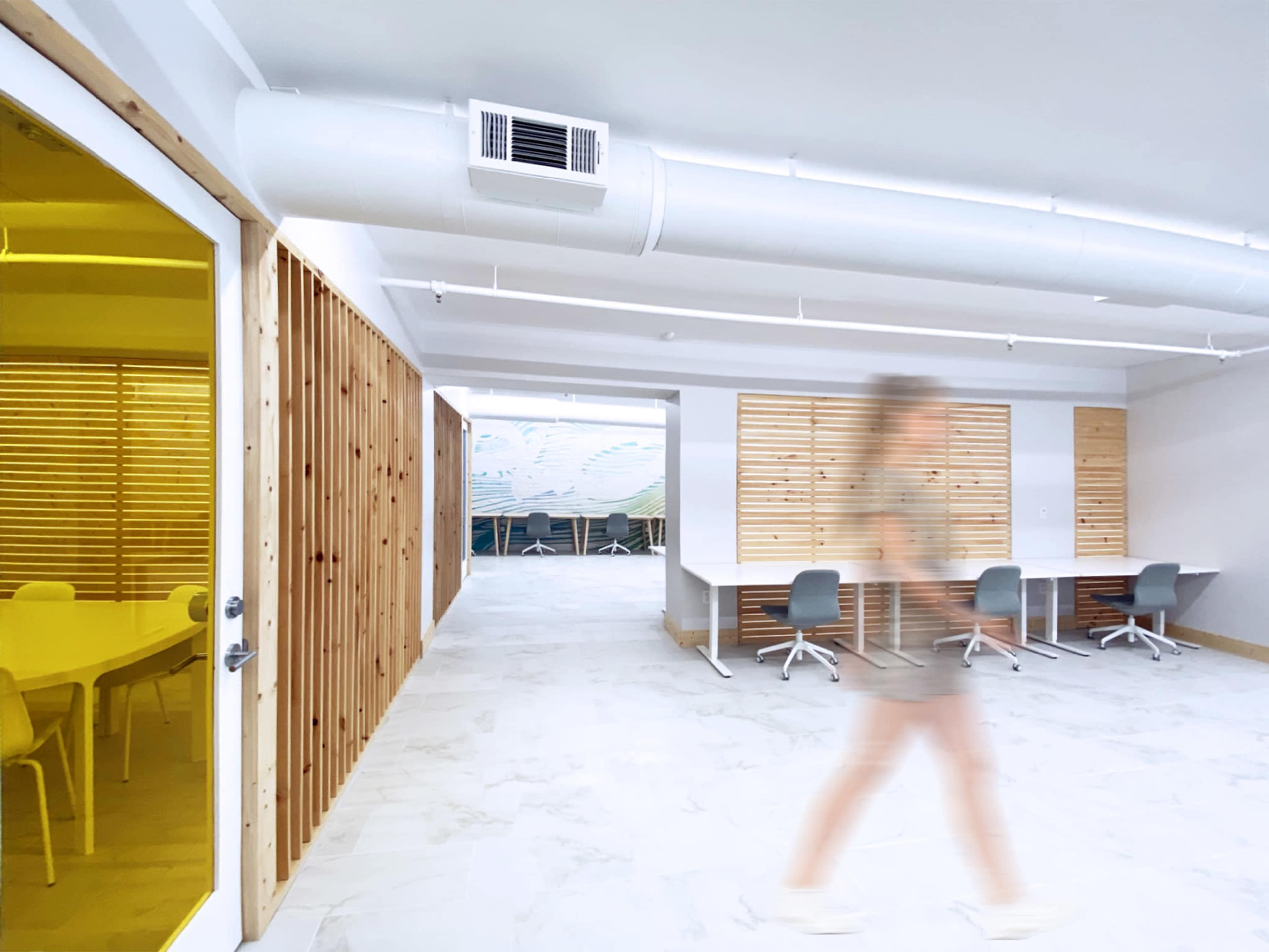 A person walks through a modern office space featuring wooden accent walls and minimalistic furniture.