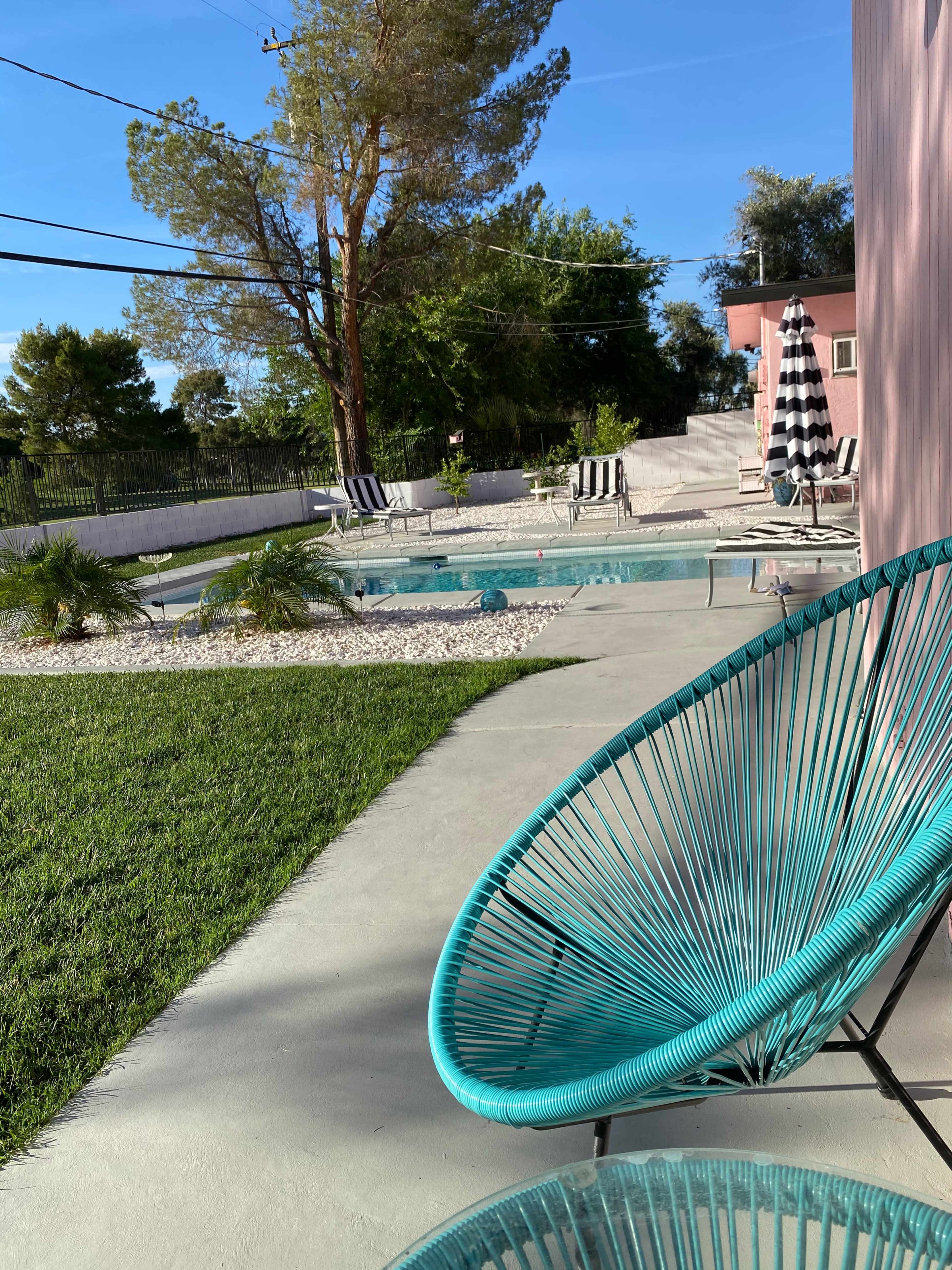 A pool area surrounded by chairs and lounge chairs, with a green lawn and a concrete pathway leading through the space.