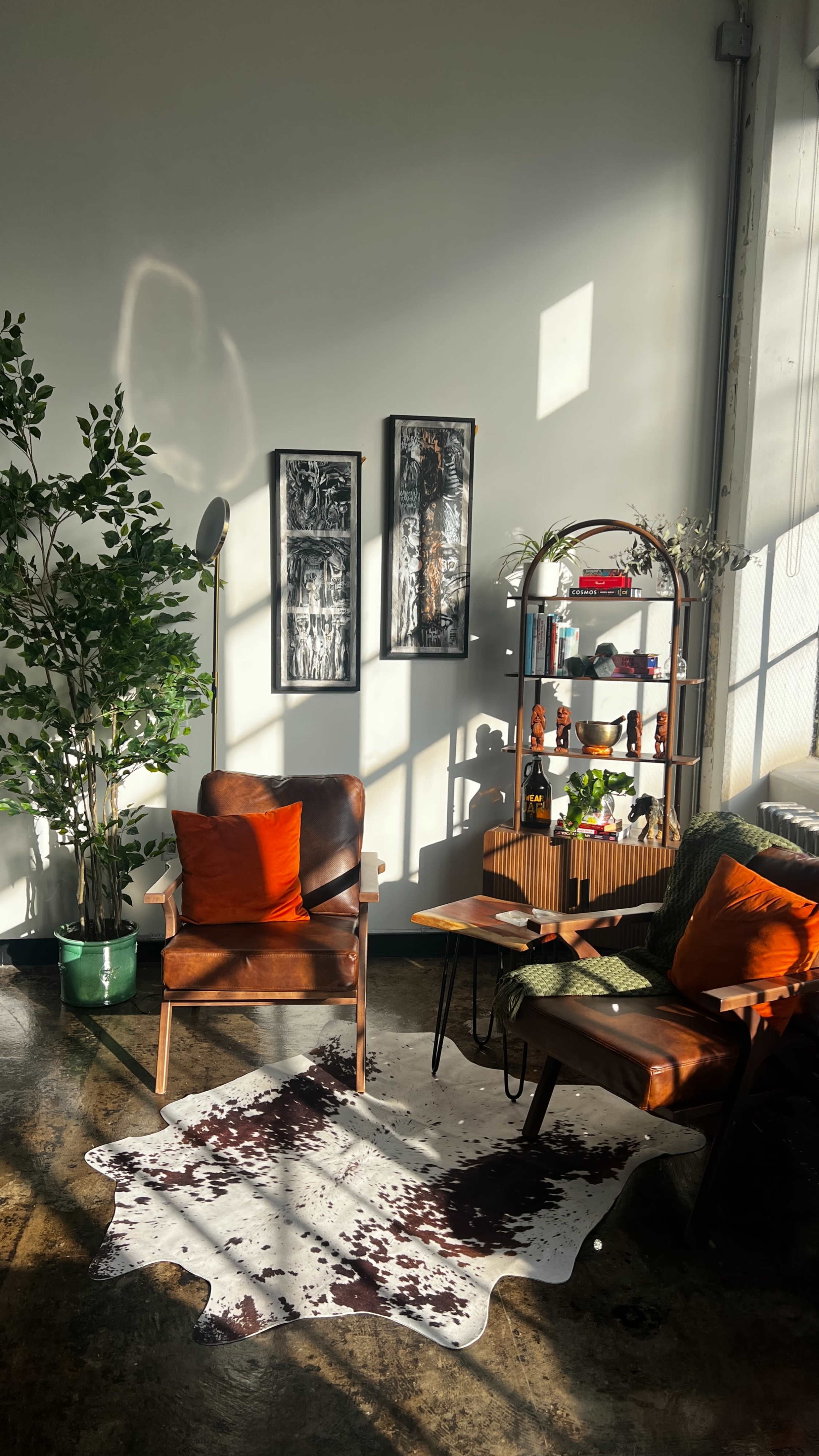 The image shows a well-lit cozy living room with a brown leather armchair, a wooden side table, and a green potted plant beside a shelf displaying various decorative items.