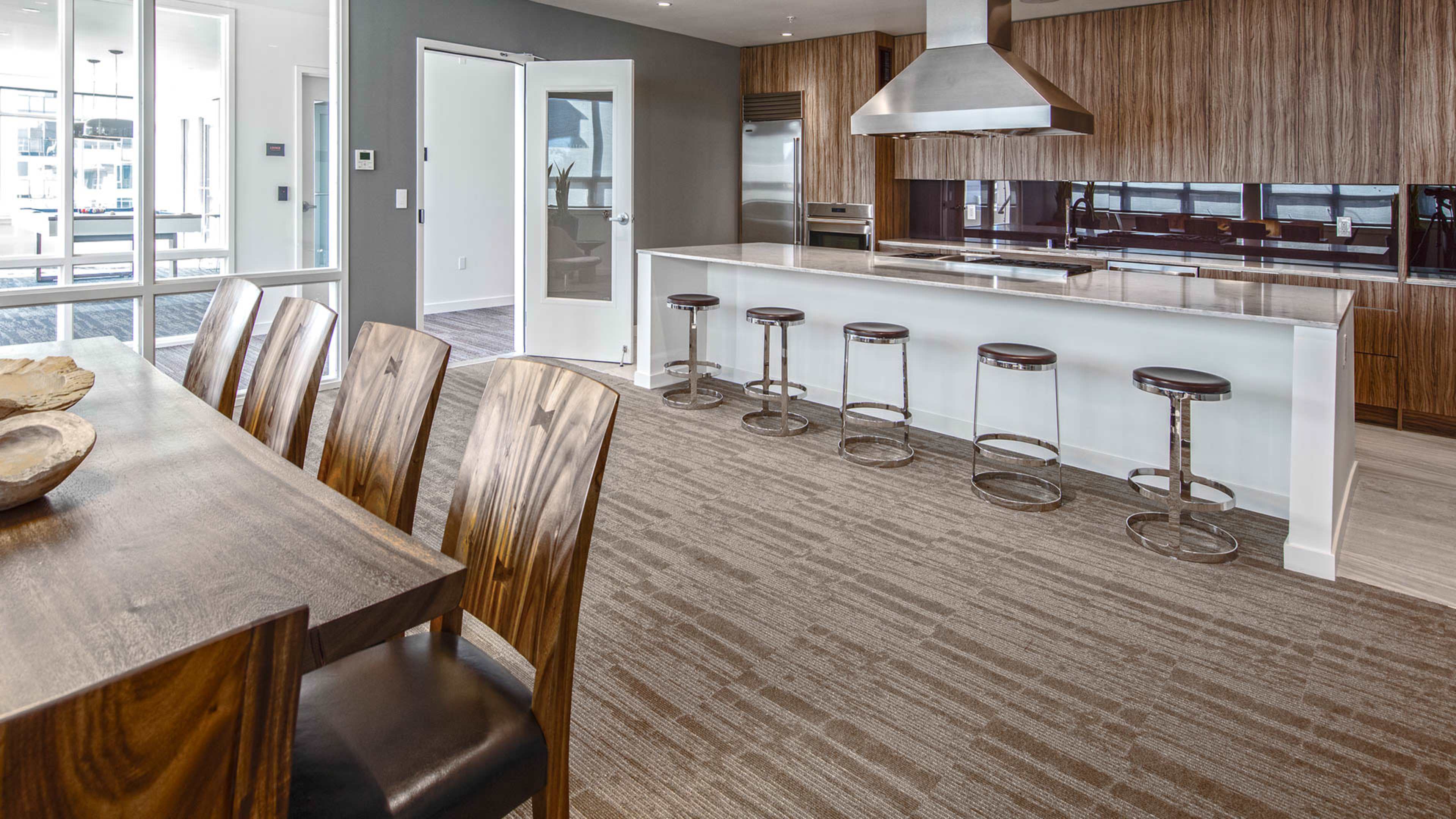 A modern kitchen and dining area featuring a long wooden table, high-backed chairs, a sleek kitchen island with stools, and large windows letting in natural light.