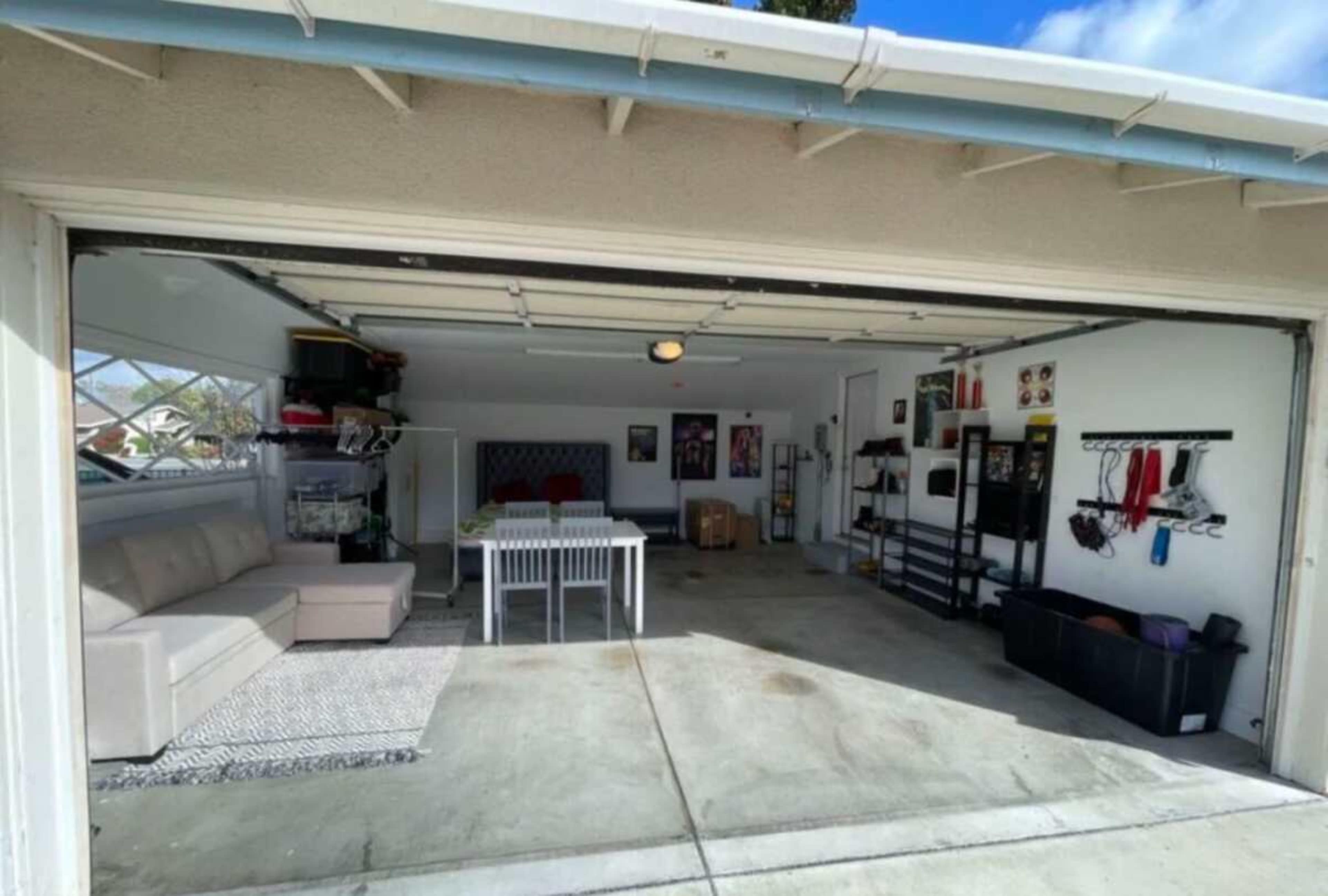 The image shows a two-car garage with a beige sectional sofa, a white dining table, and various storage units along the walls.