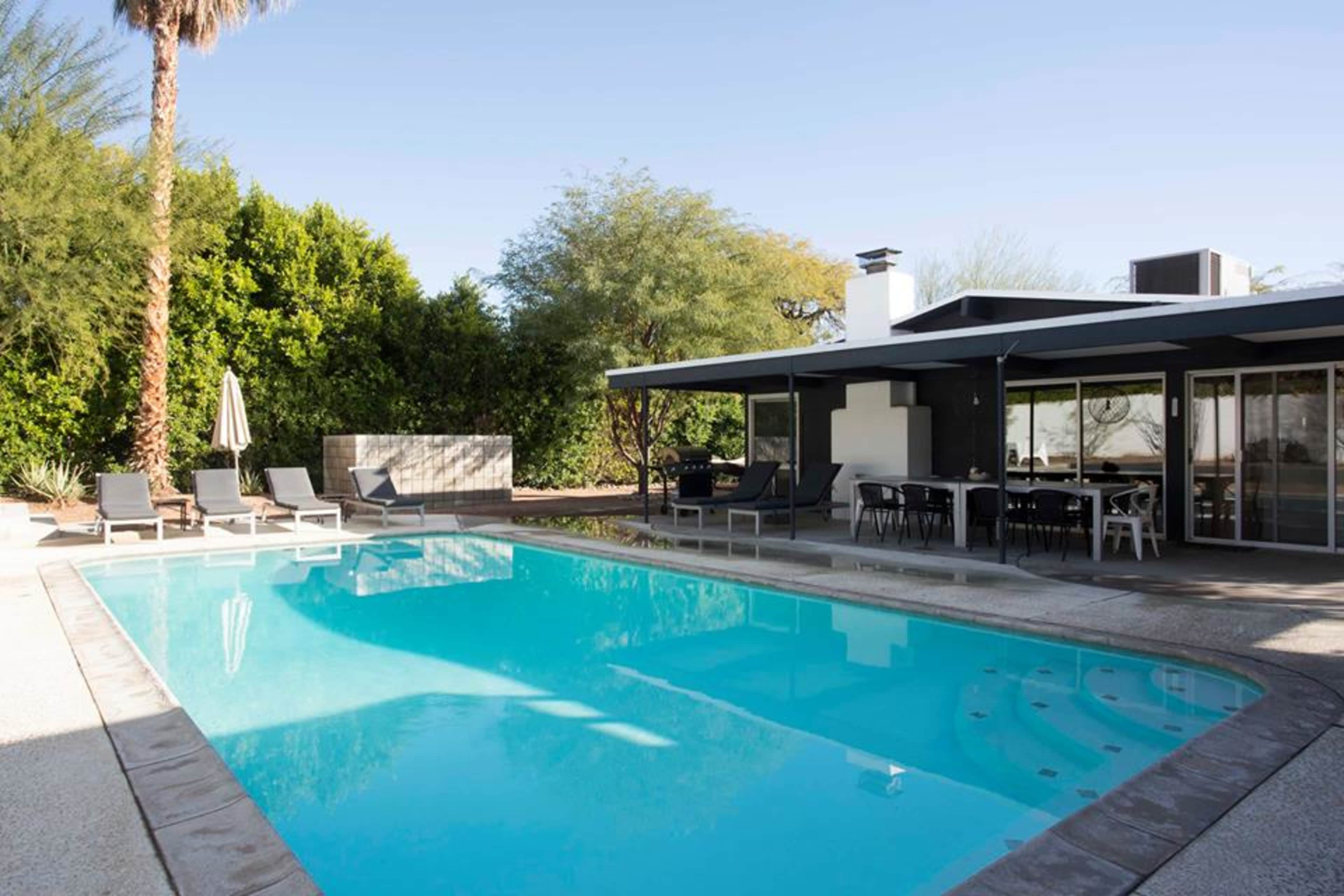 A modern backyard with a swimming pool and lounge chairs, surrounded by landscaping and a patio area.