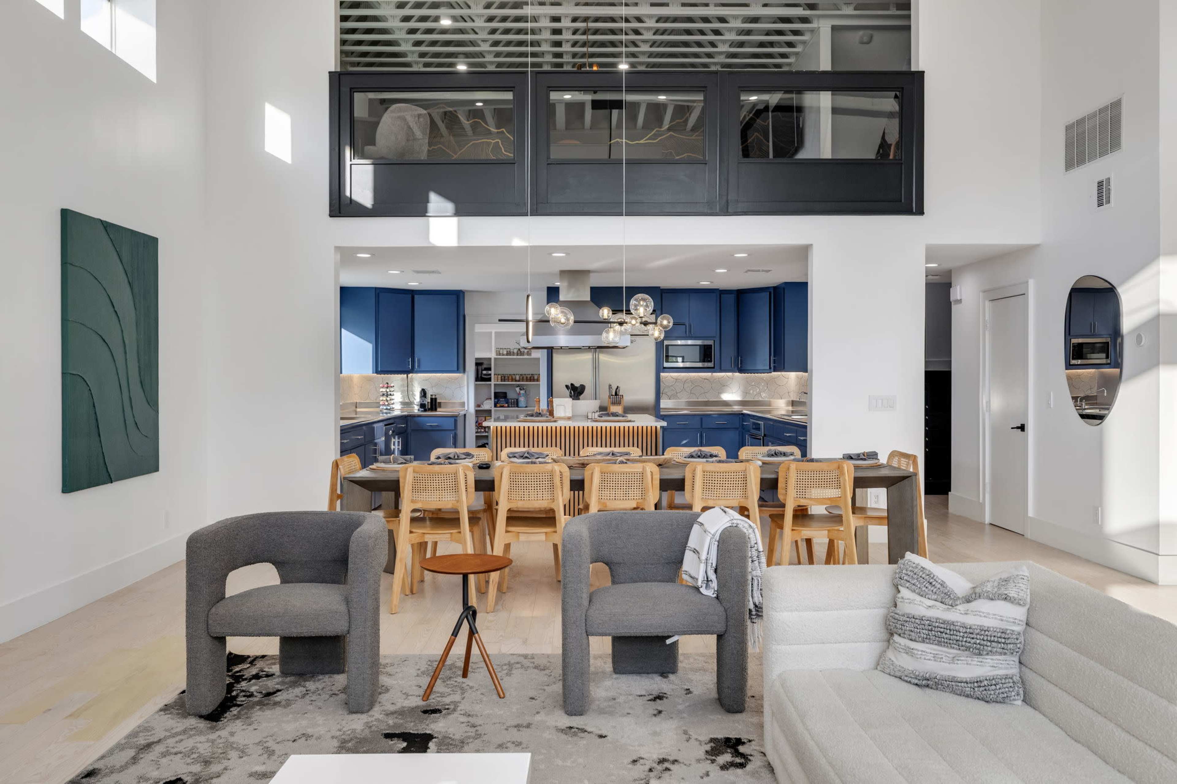 The image features a modern interior space with a dining area and kitchen, characterized by blue cabinetry, a wooden dining table, and an open layout.