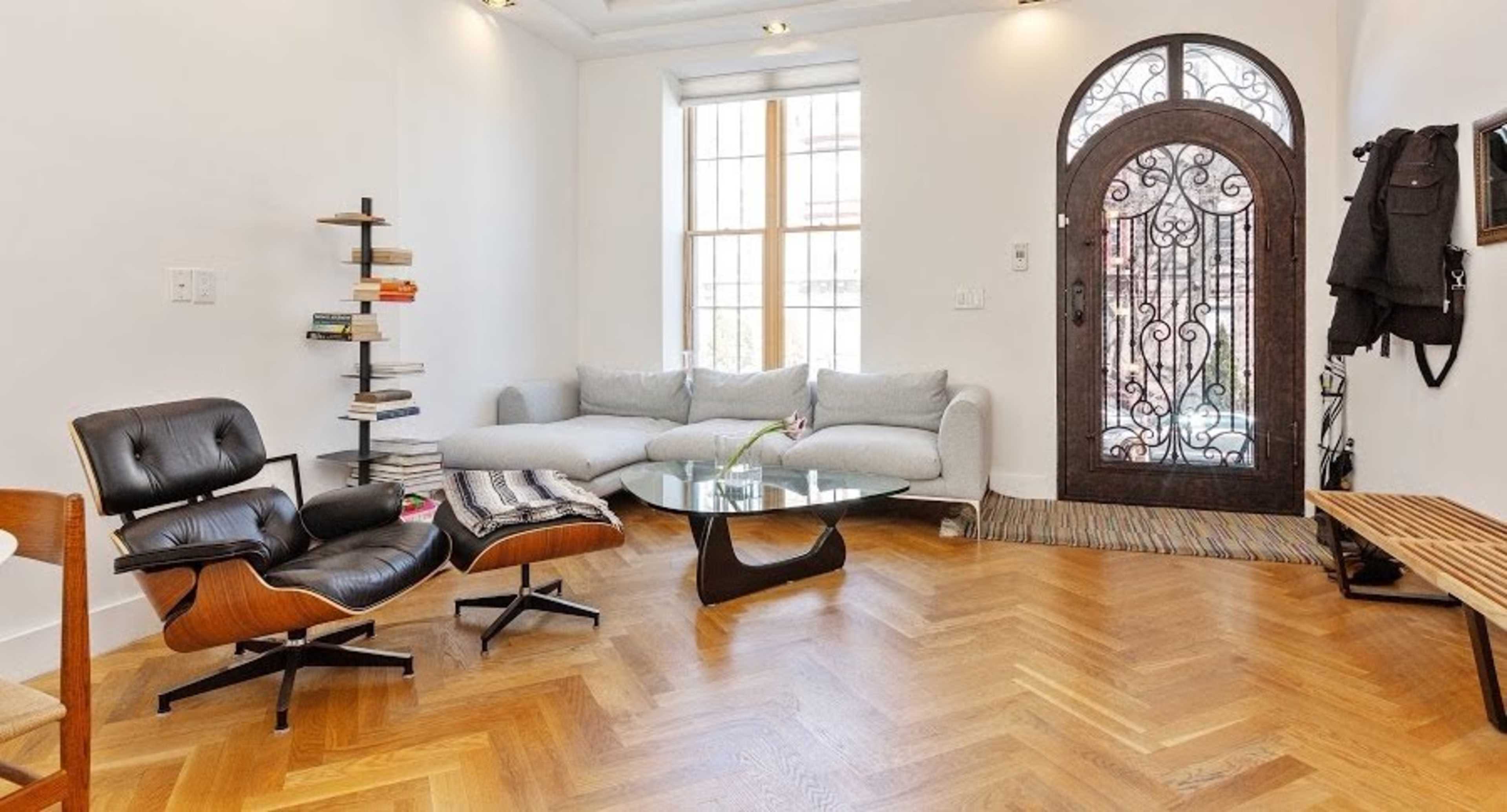 A modern living room featuring a gray sofa, a glass coffee table, a stylish armchair, and a decorative entrance door with intricate ironwork.