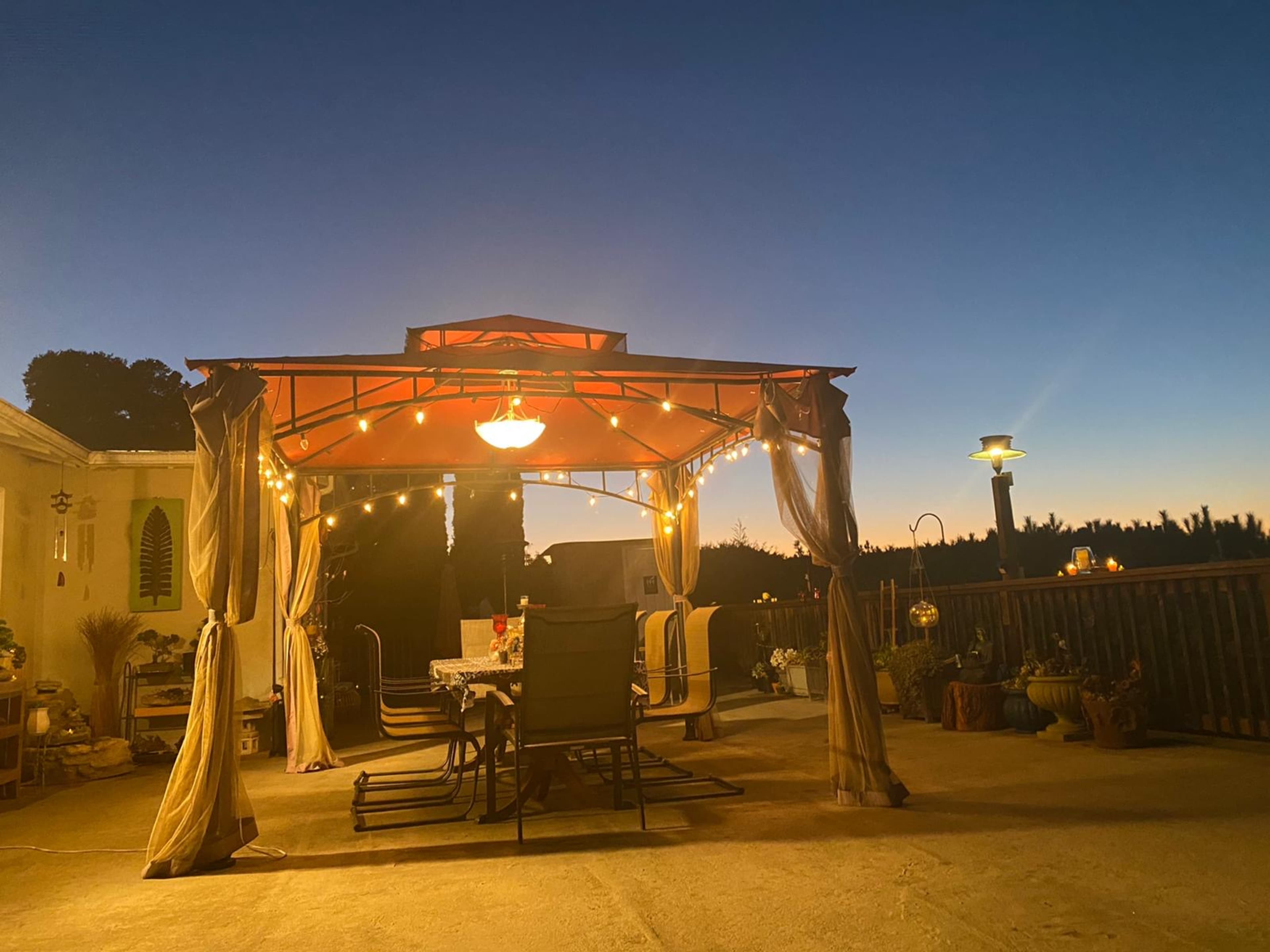 A gazebo with string lights is set up on a patio, overlooking a horizon at dusk.