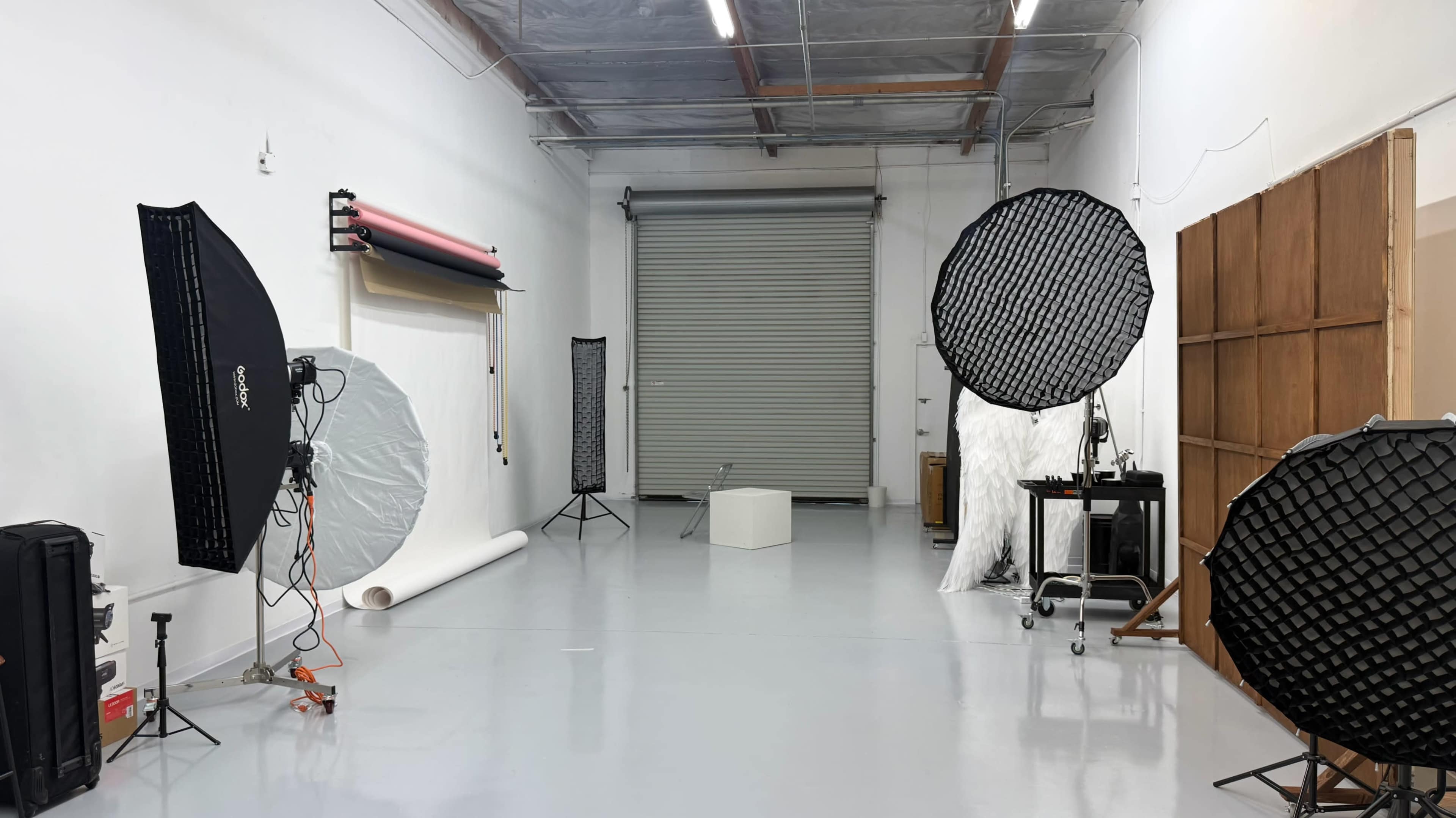 The image shows a photography studio equipped with various lighting setups, backdrops, and a roll of paper in a clean, well-lit space.