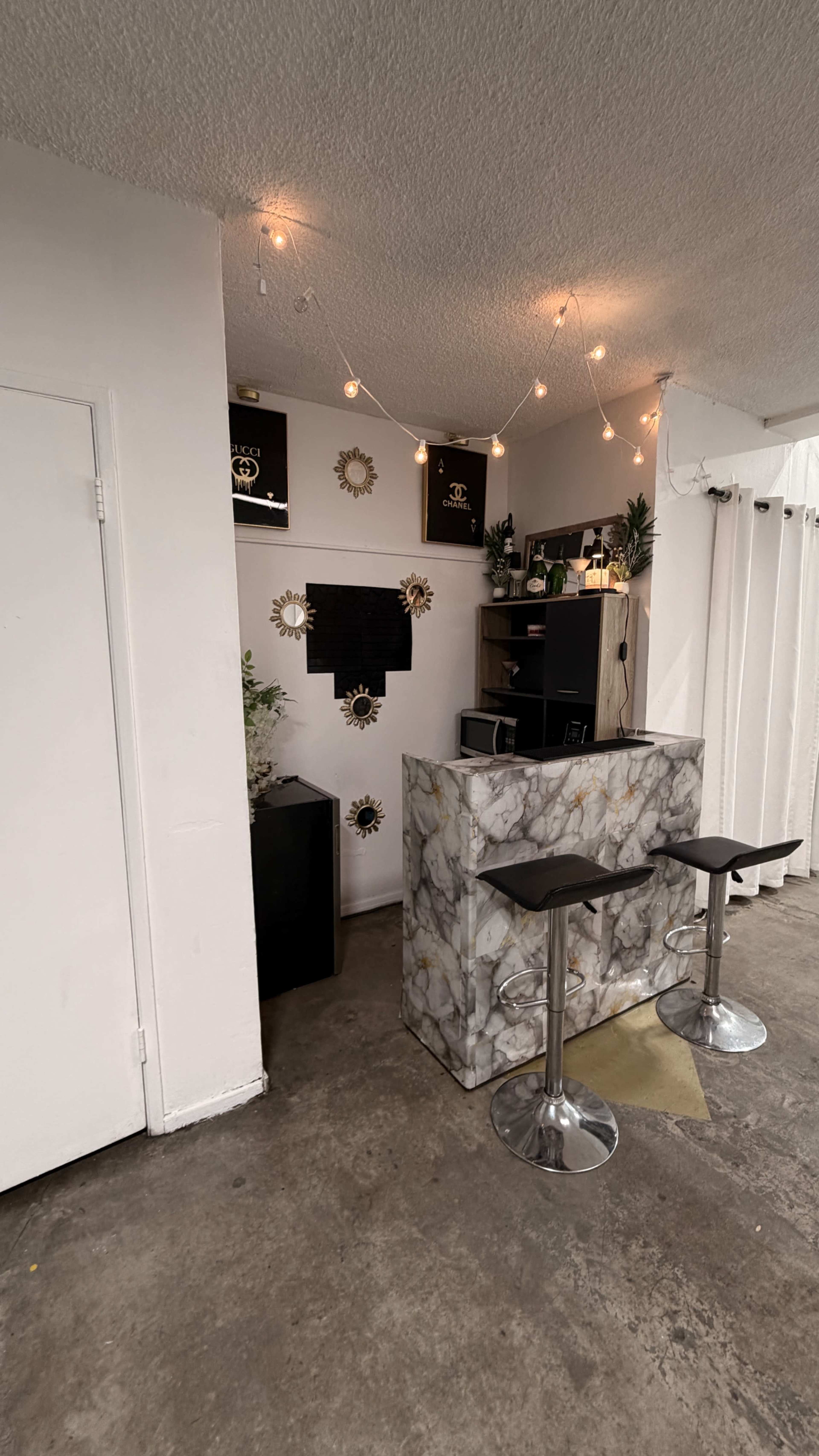 The image shows a small reception area with a marbled front desk, two stools, and shelves adorned with decorative items and plants.