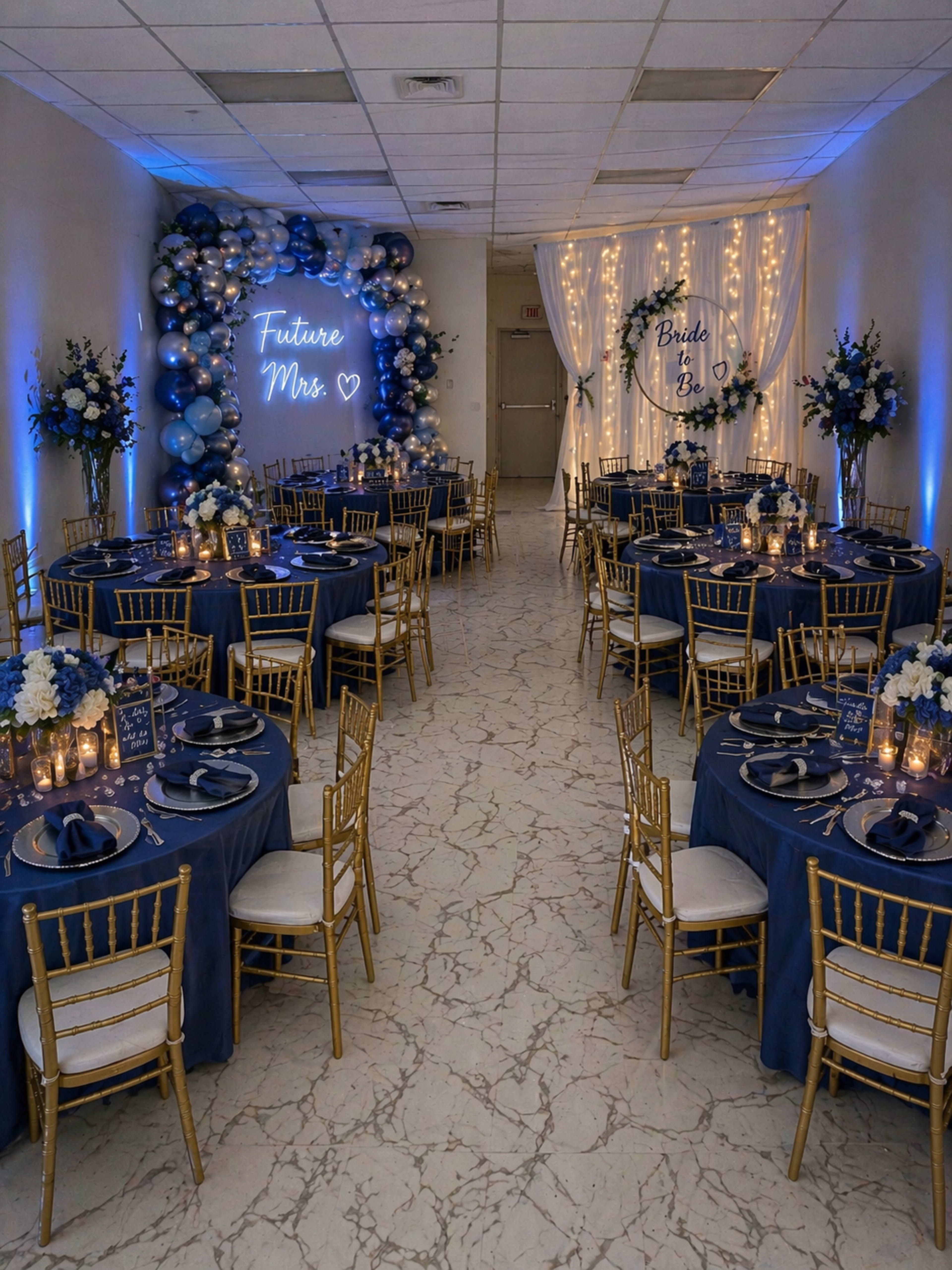 The image shows a banquet hall decorated for a bridal event, featuring round tables with dark blue tablecloths, gold chairs, and floral arrangements, along with a backdrop of balloons and lights.