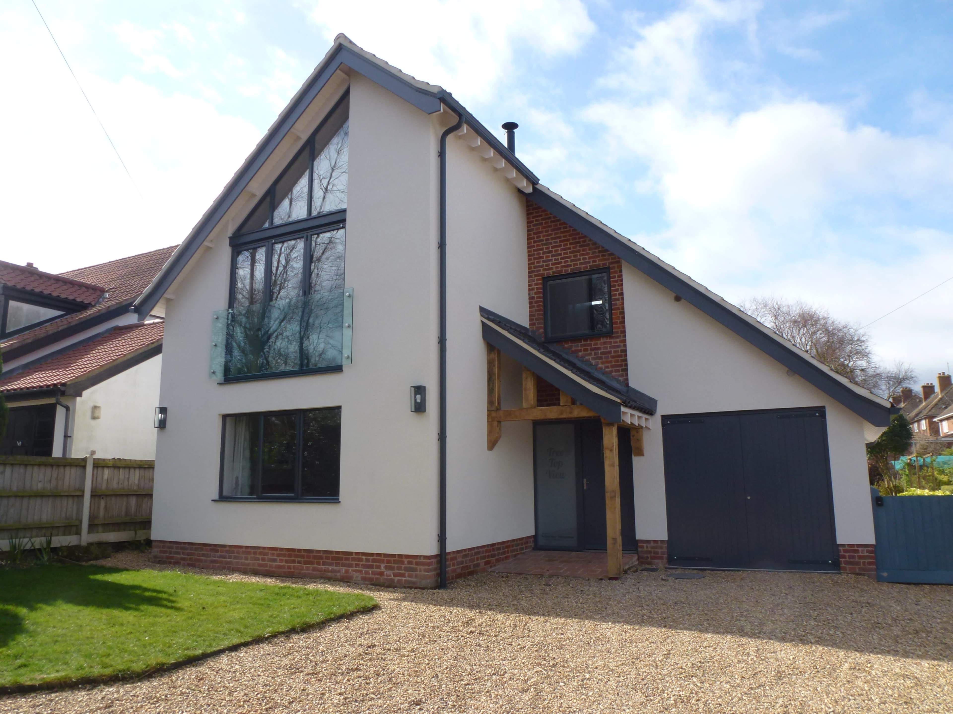 The image shows a modern two-story house with a sloped roof, large windows, and a gravel driveway.