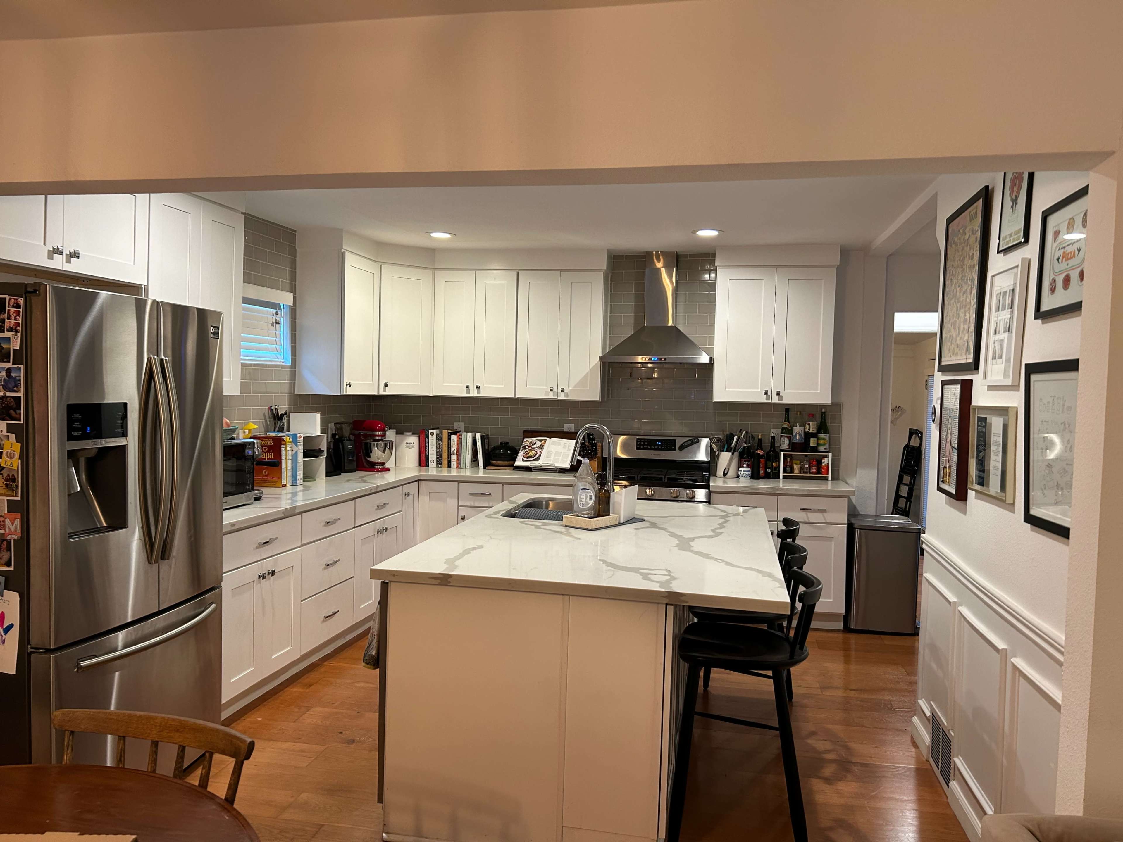 A modern kitchen featuring white cabinetry, a marble-topped island with bar stools, and stainless steel appliances.
