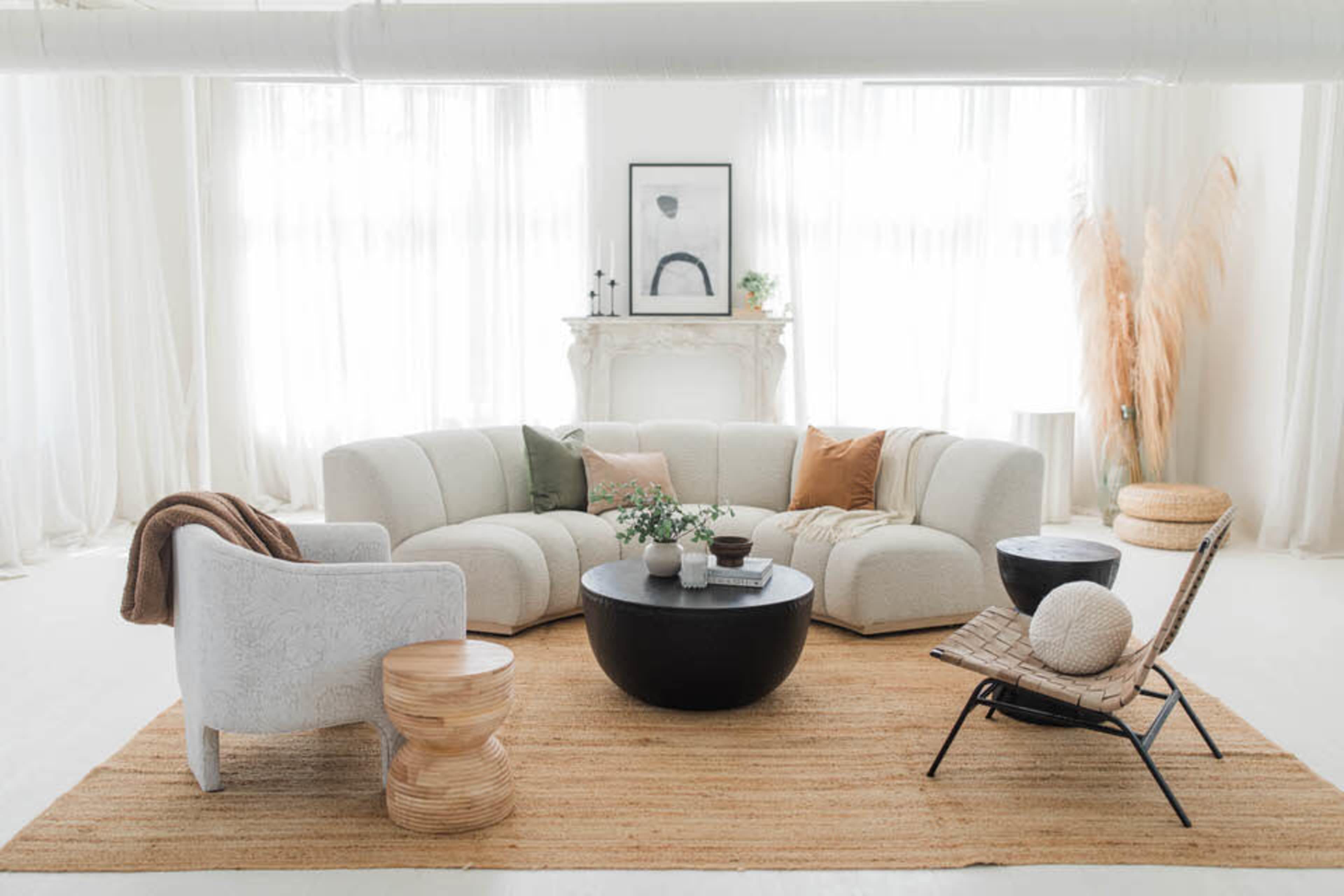 The image shows a modern living room with a curved white sofa, a round black coffee table, and various decorative elements, all arranged on a light-colored rug.