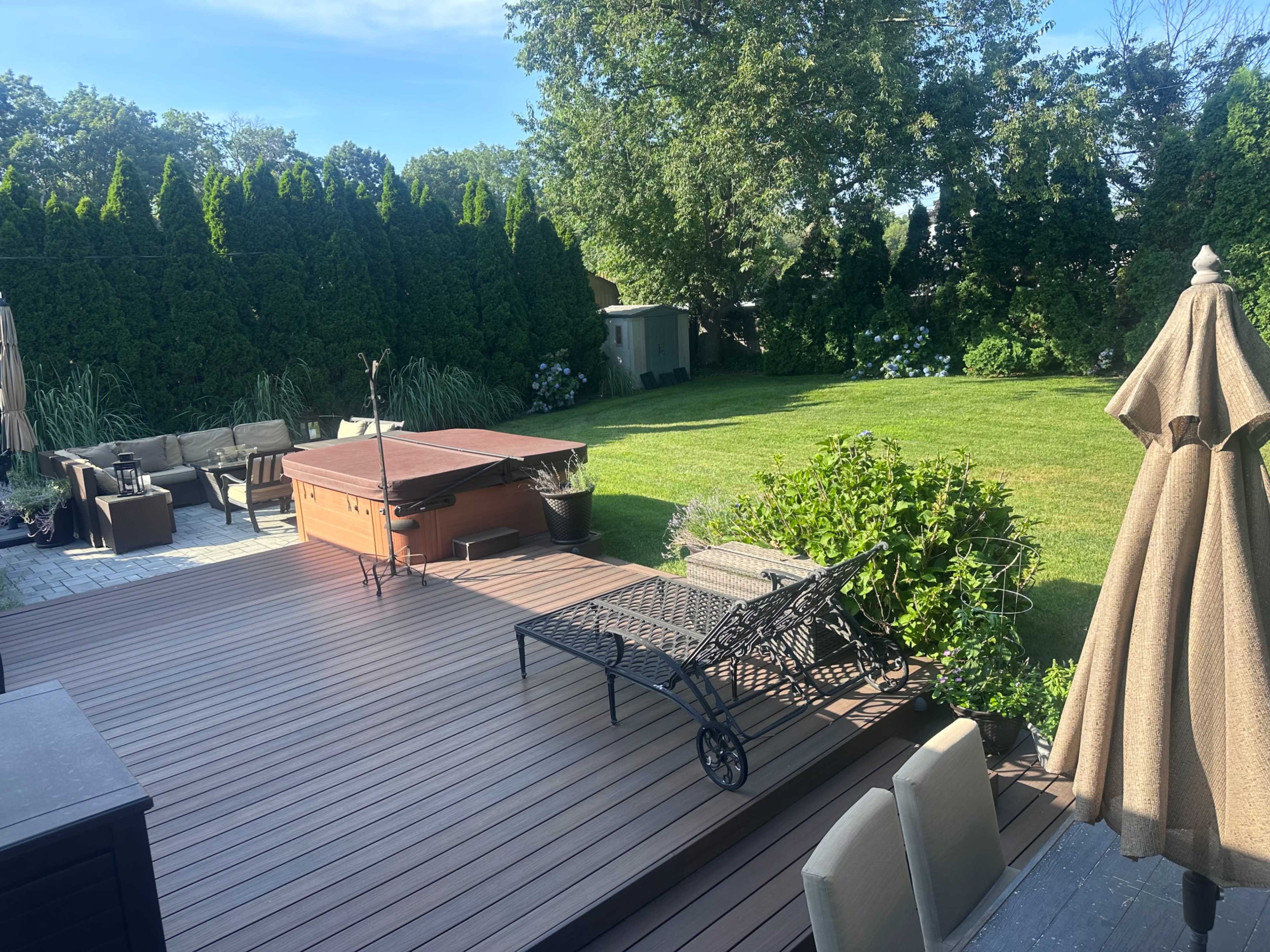 The image shows a spacious backyard with a wooden deck, a hot tub, outdoor furniture, and well-maintained grass.
