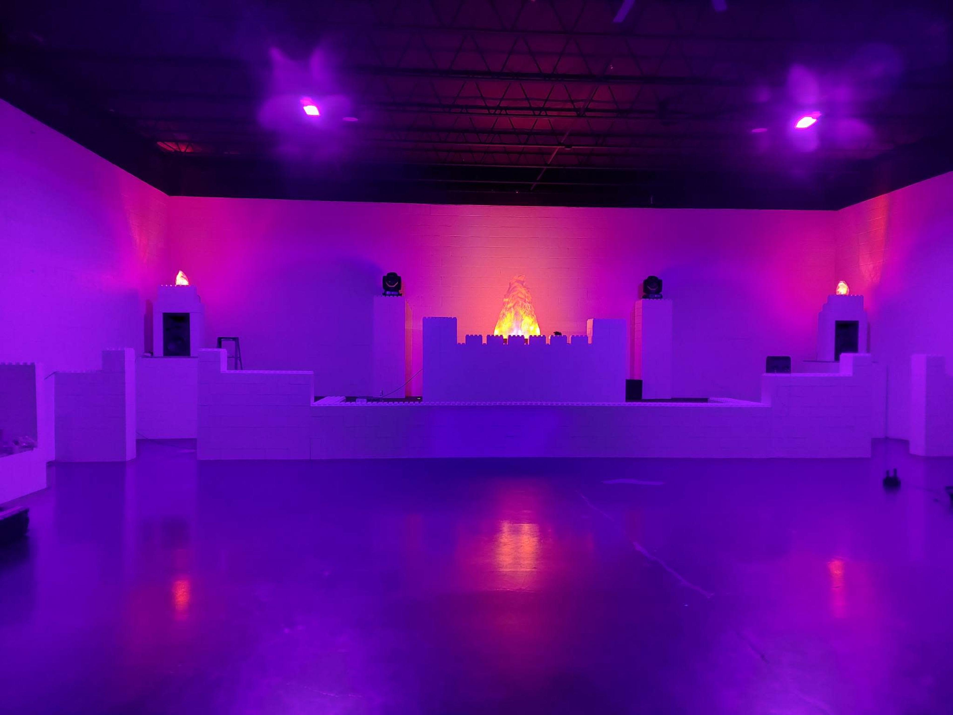An indoor space with white structures arranged to resemble a castle, illuminated by purple and orange lighting.