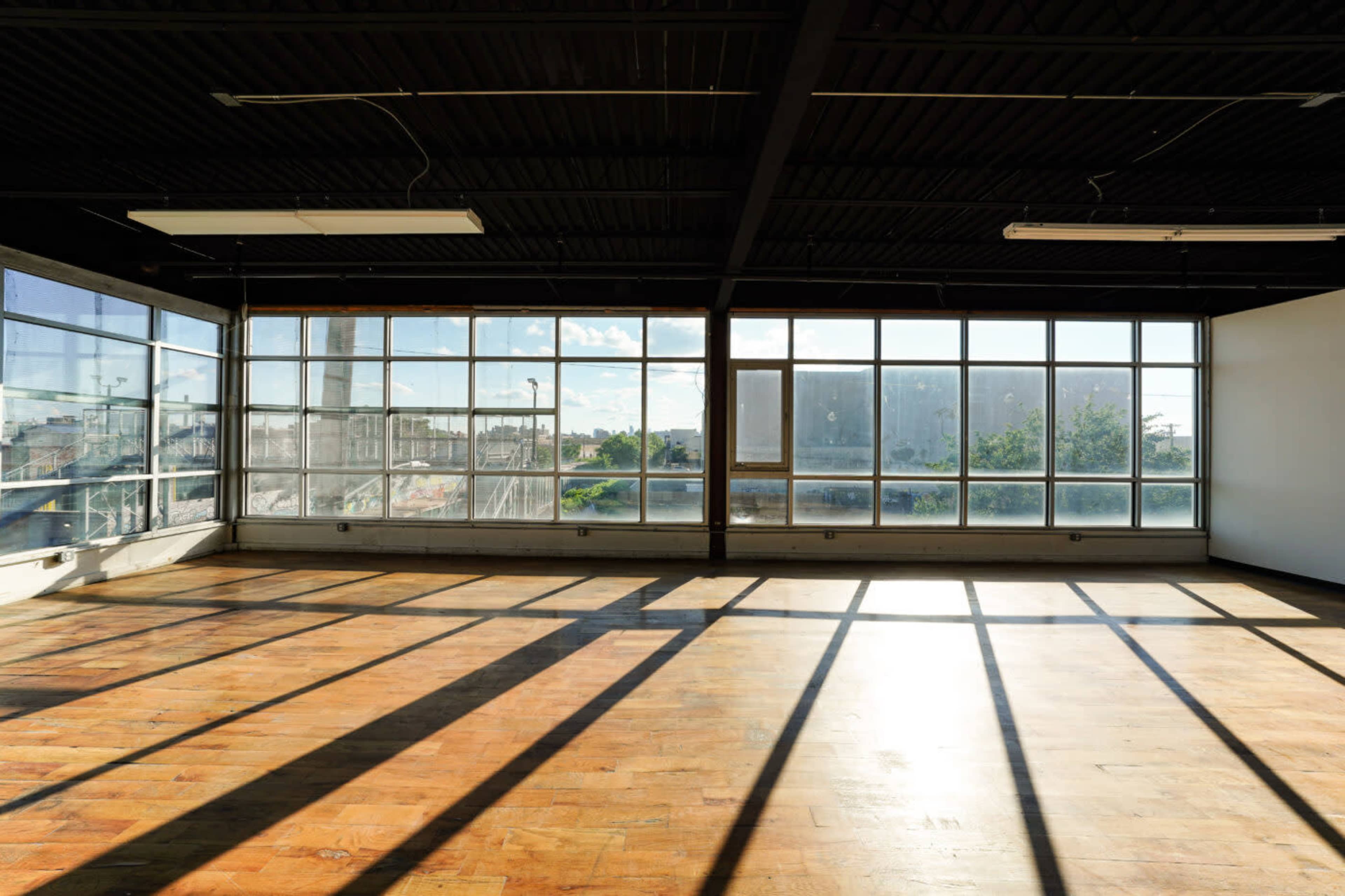 An empty room with large windows that allow sunlight to cast long shadows on the polished wooden floor.
