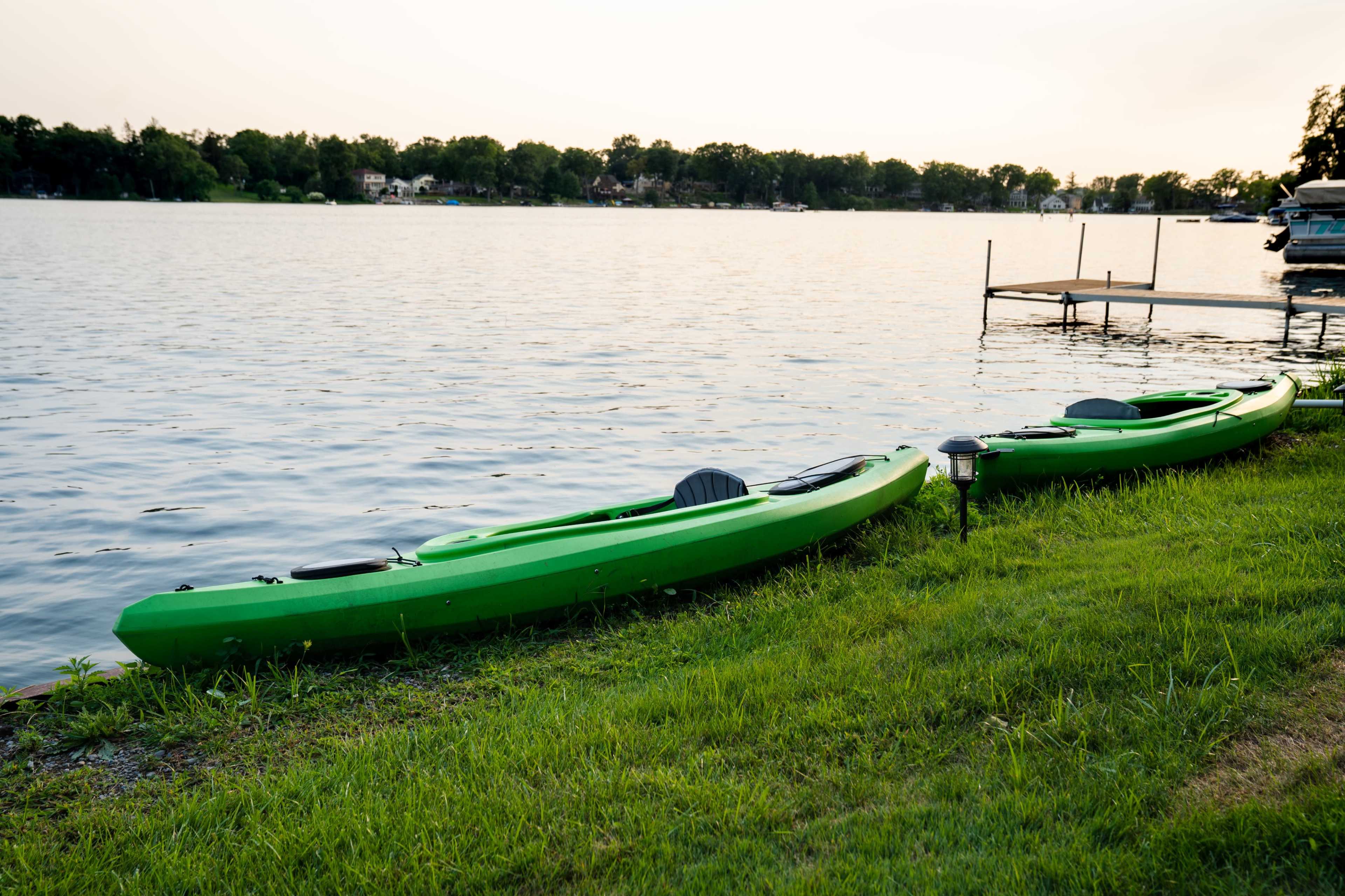 Two green kayaks are positioned on the grassy shore next to a calm lake at sunset.