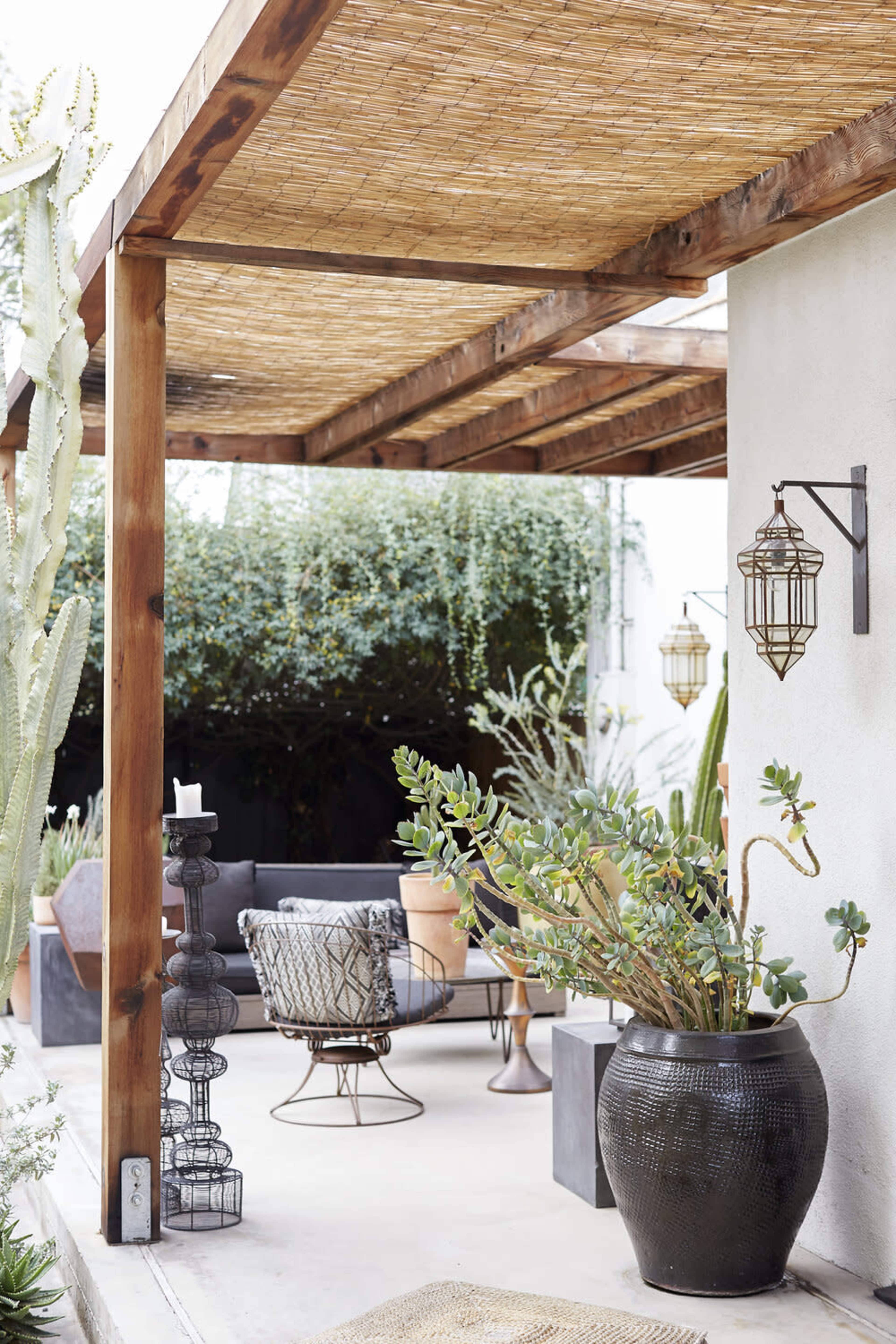 A shaded outdoor seating area with plants, modern furniture, and decorative lighting under a wooden pergola.