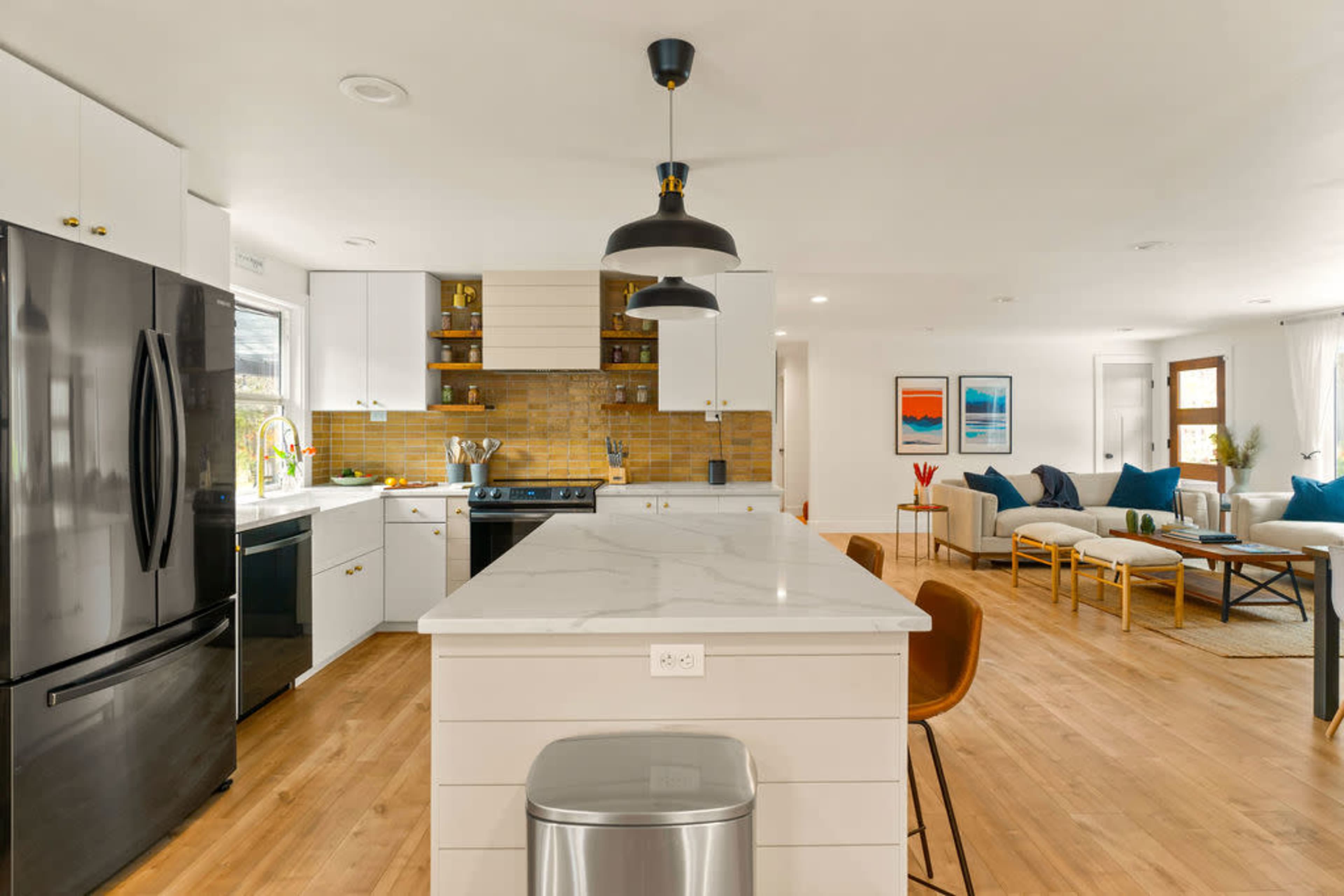 A modern kitchen with a central island and a black refrigerator, featuring white cabinets and a warm-toned backsplash.