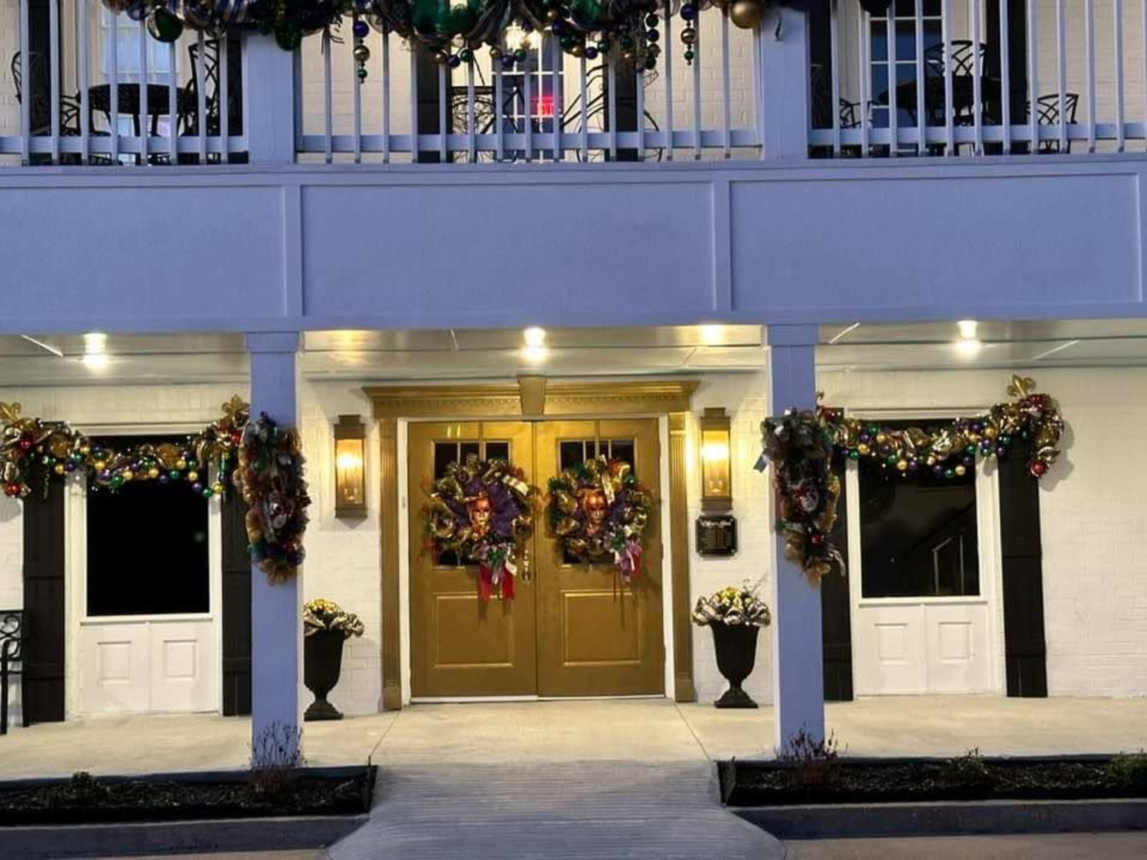 The entrance features double gold doors adorned with festive wreaths and decorations, flanked by planters and lit by wall sconces.