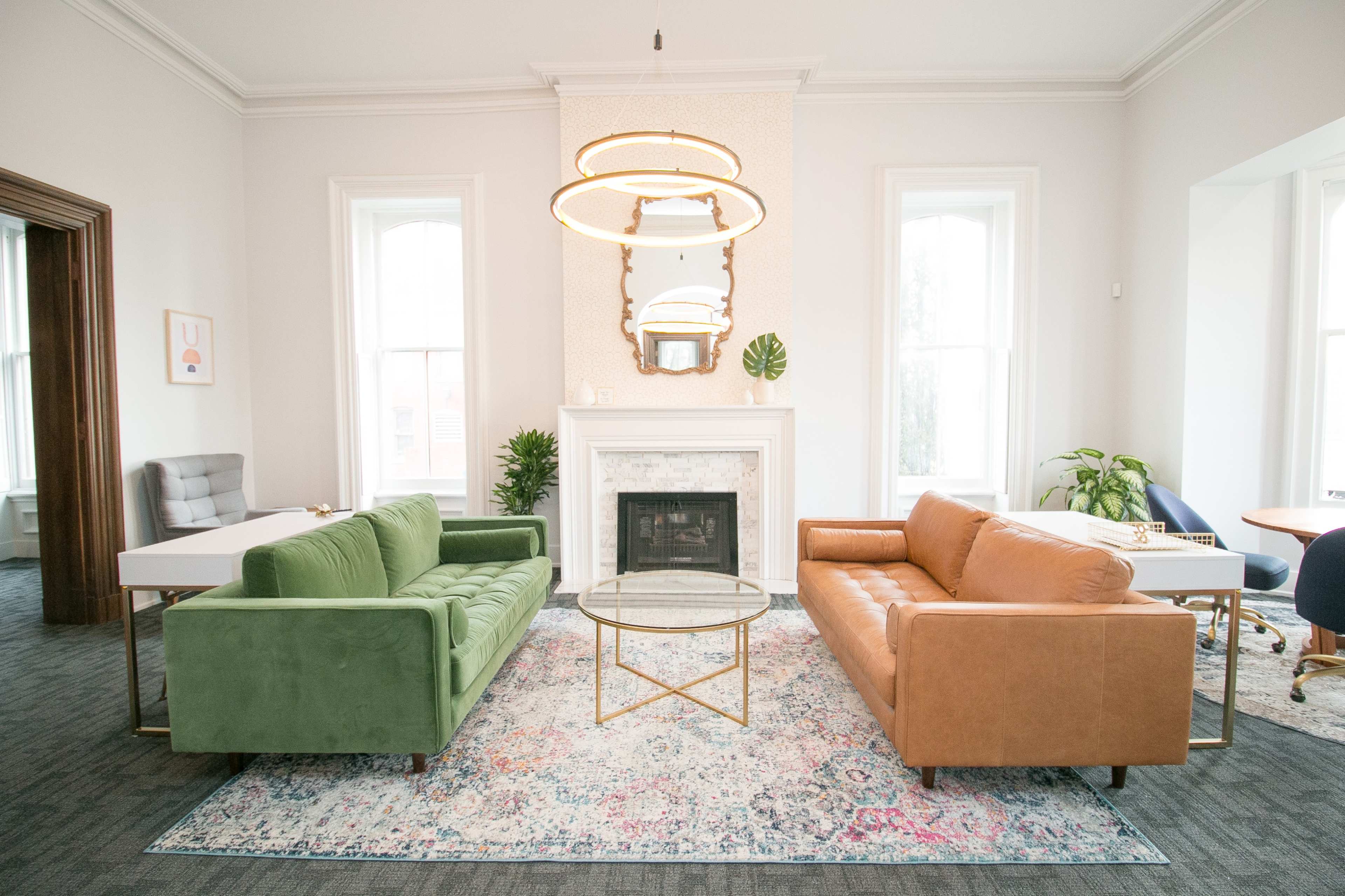 A brightly lit room furnished with a green sofa, a brown leather sofa, a circular coffee table, and a decorative fireplace.