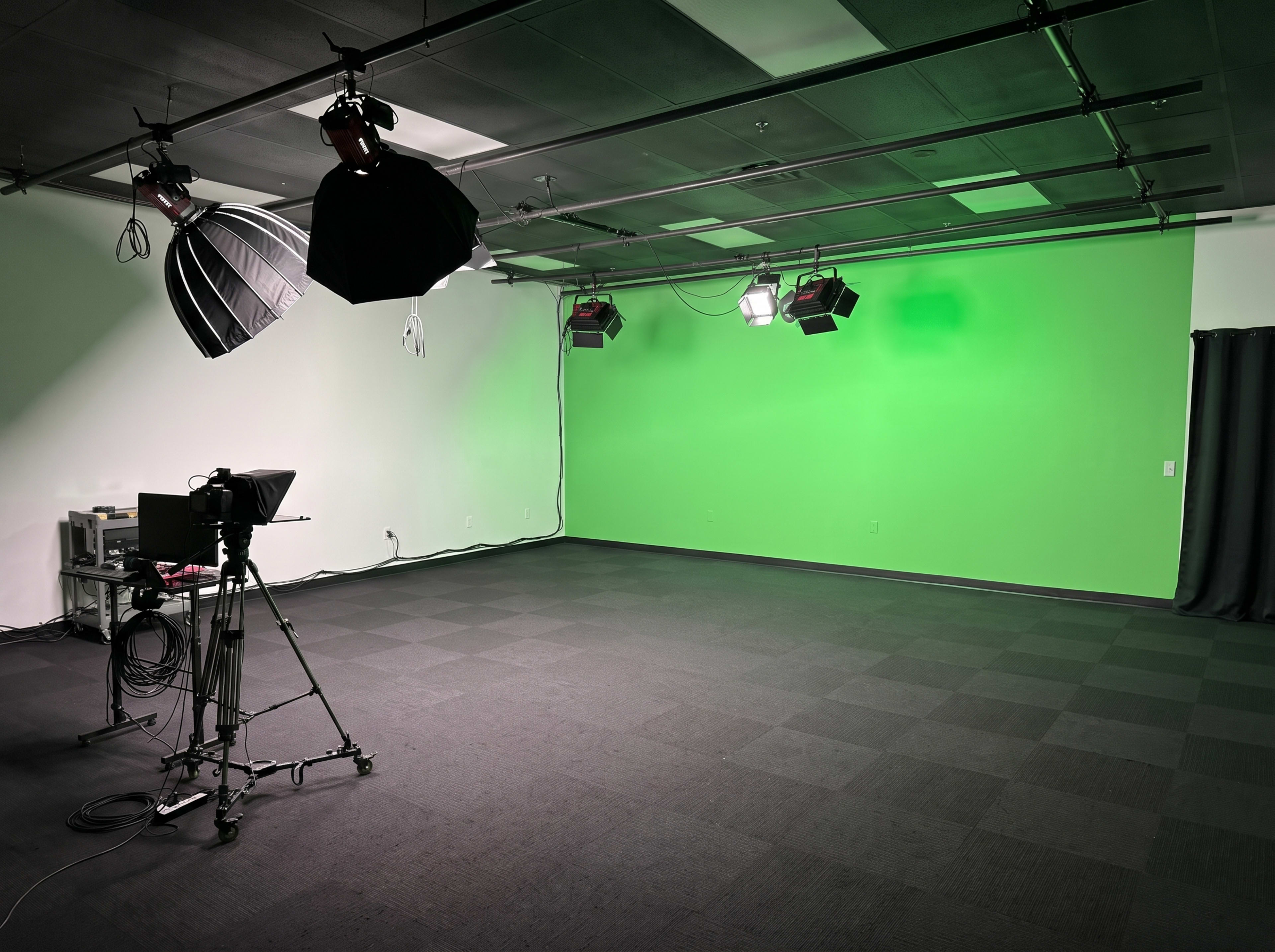 The image shows an empty studio space with a green backdrop, equipped with lighting and a camera on a tripod.