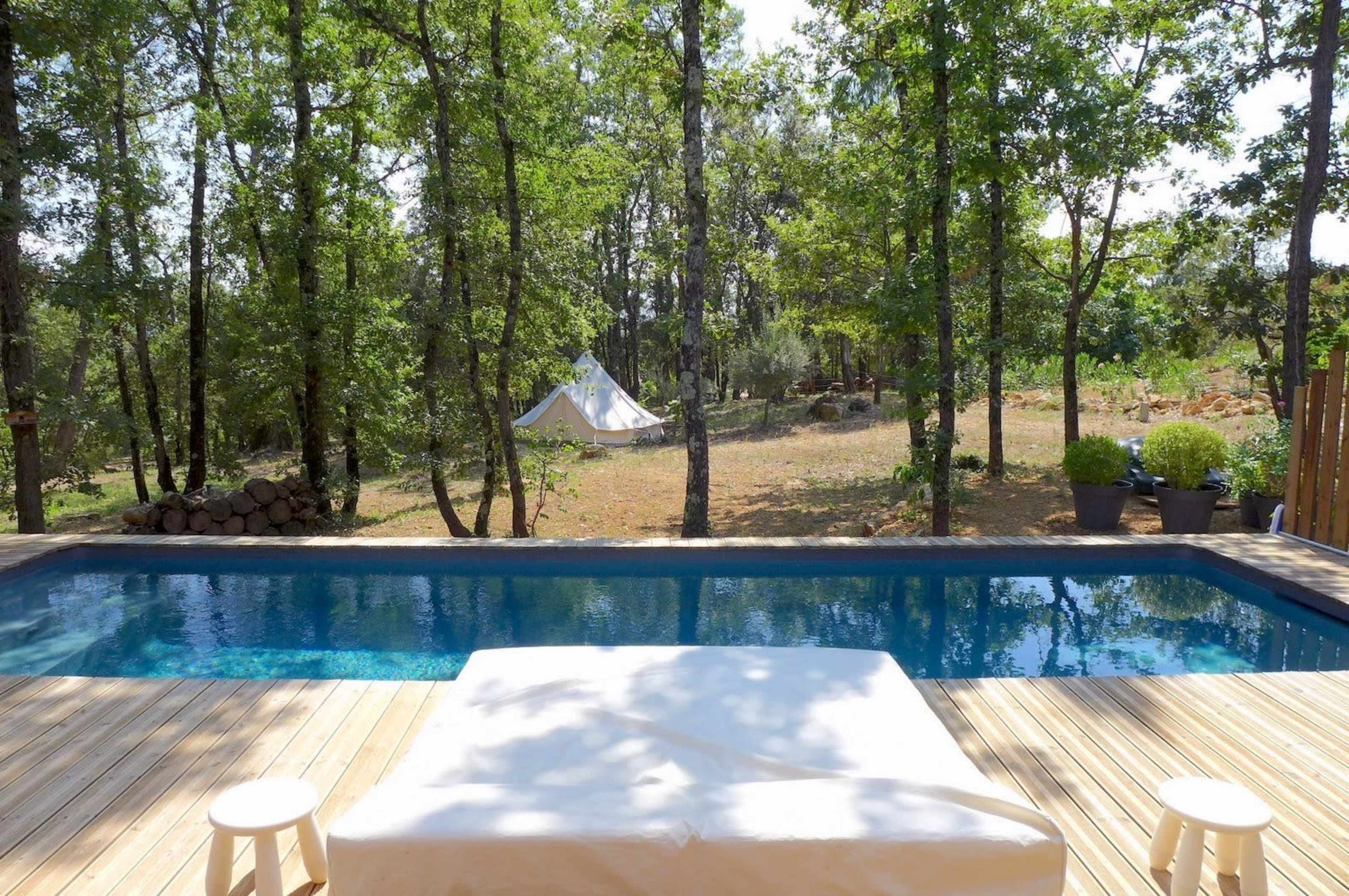 A swimming pool is set on a wooden deck surrounded by trees and a tent in the background.