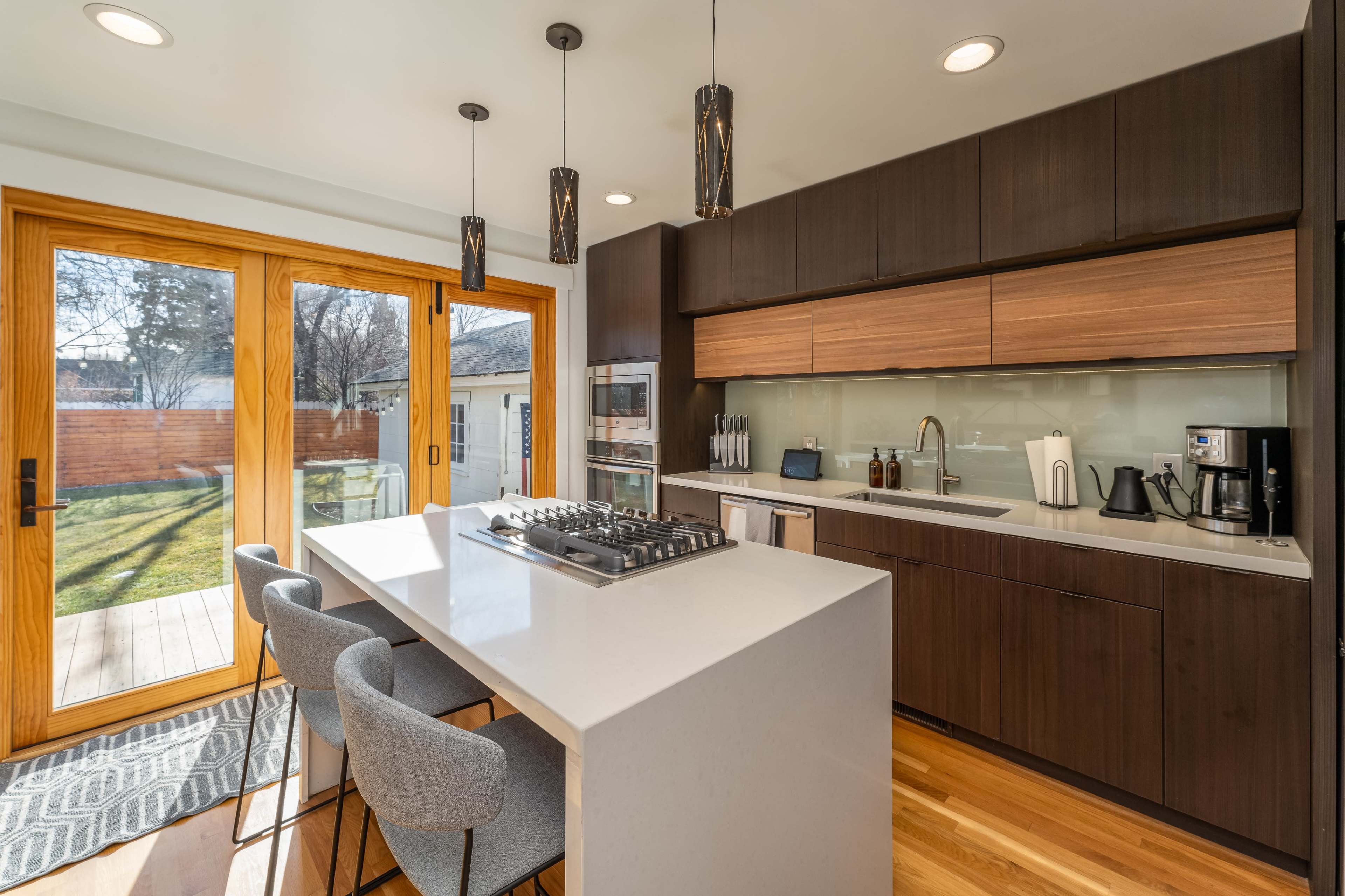 A modern kitchen features a central island with bar seating, sleek cabinetry, and large glass doors that open to an outdoor space.