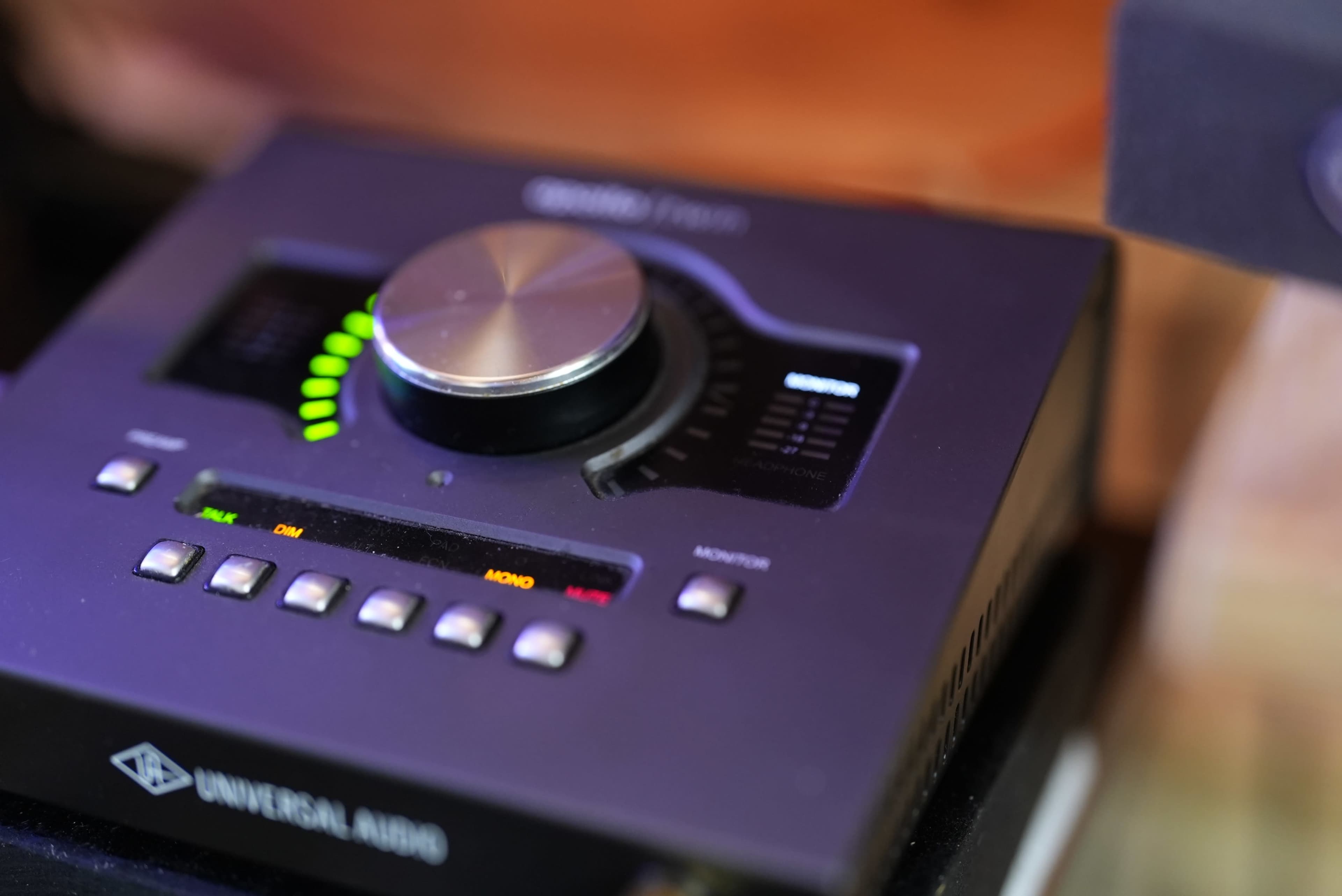 The image shows a Universal Audio audio interface featuring a large knob and LED level meters.