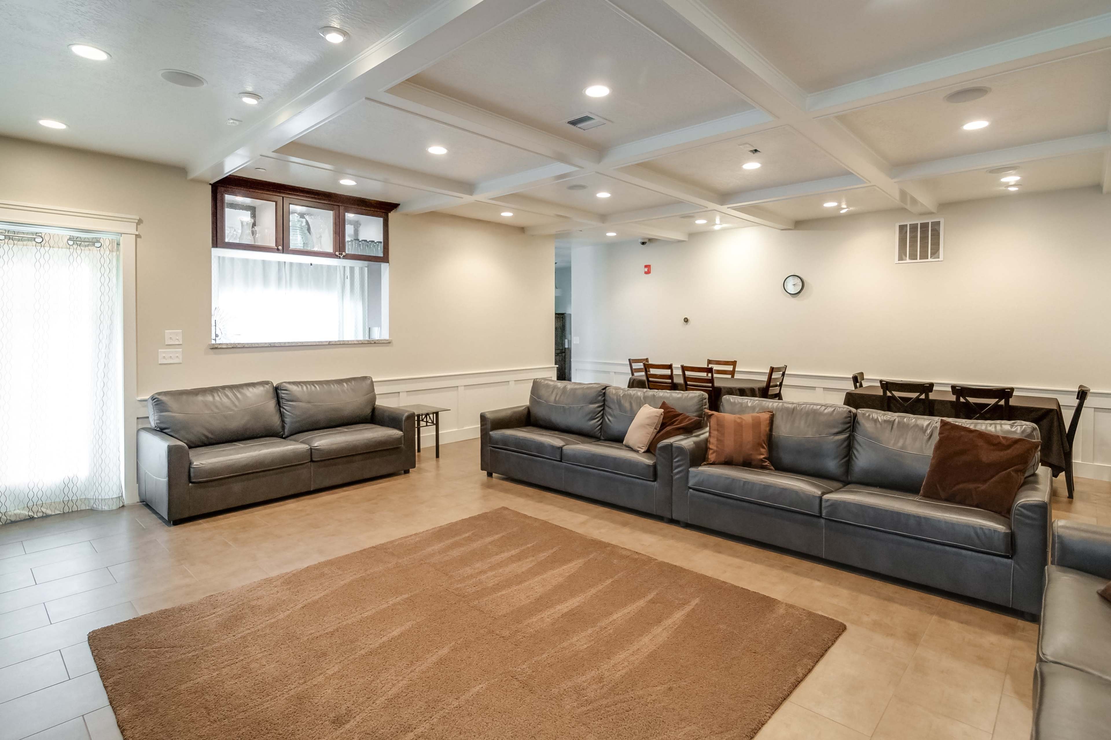 A spacious living area features gray sofas arranged around a light-colored rug, with a dining table visible in the background.