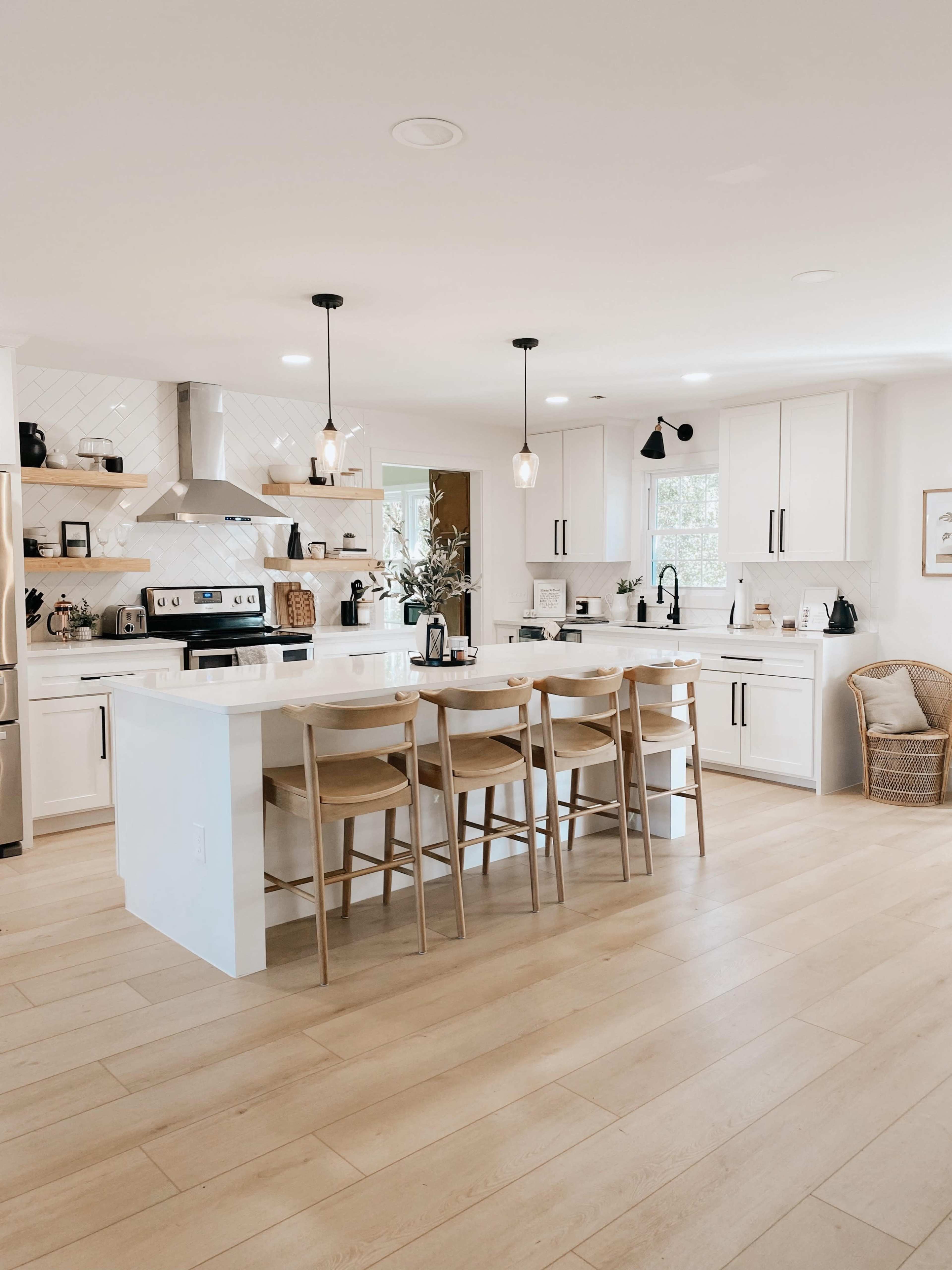 A modern kitchen features white cabinetry, a central island with seating, and stainless steel appliances.