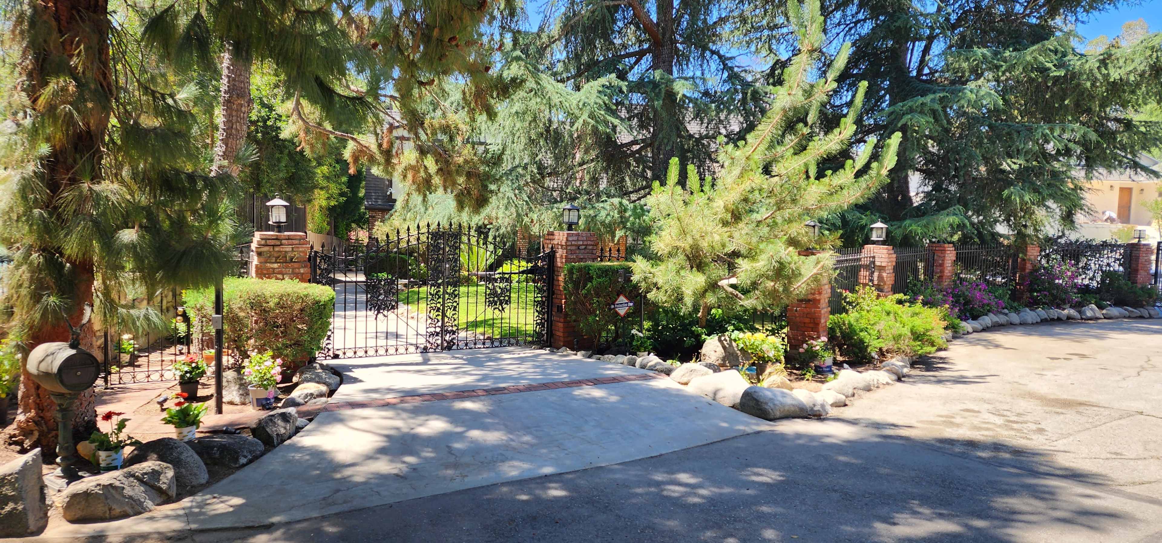 A gated entrance to a property, framed by tall trees and colorful flower beds along the driveway.